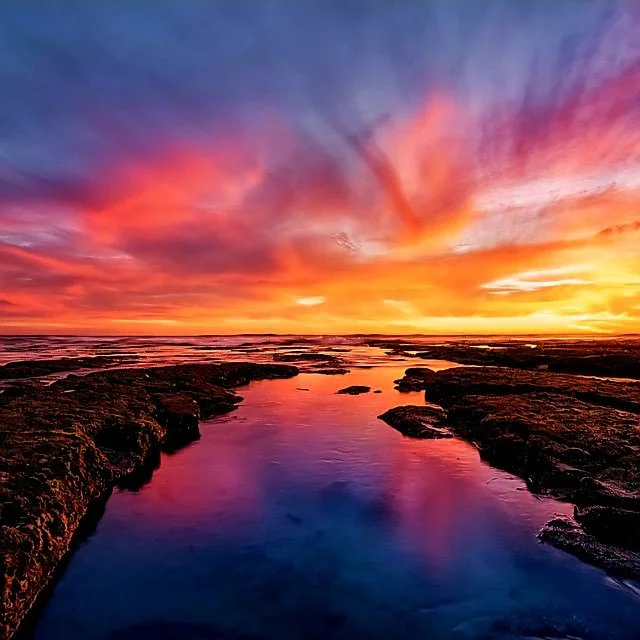 Colorful sunset over rocky shoreline with reflected sky in calm water