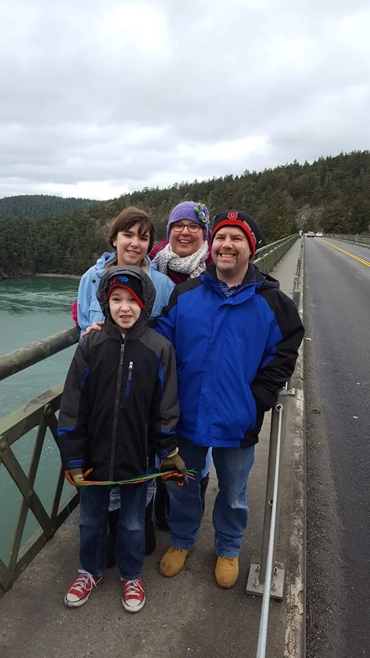 A family with Dad and Mom and two children, dressed warmly,  standing on the bridge at Point Deception Pass, Washington State.