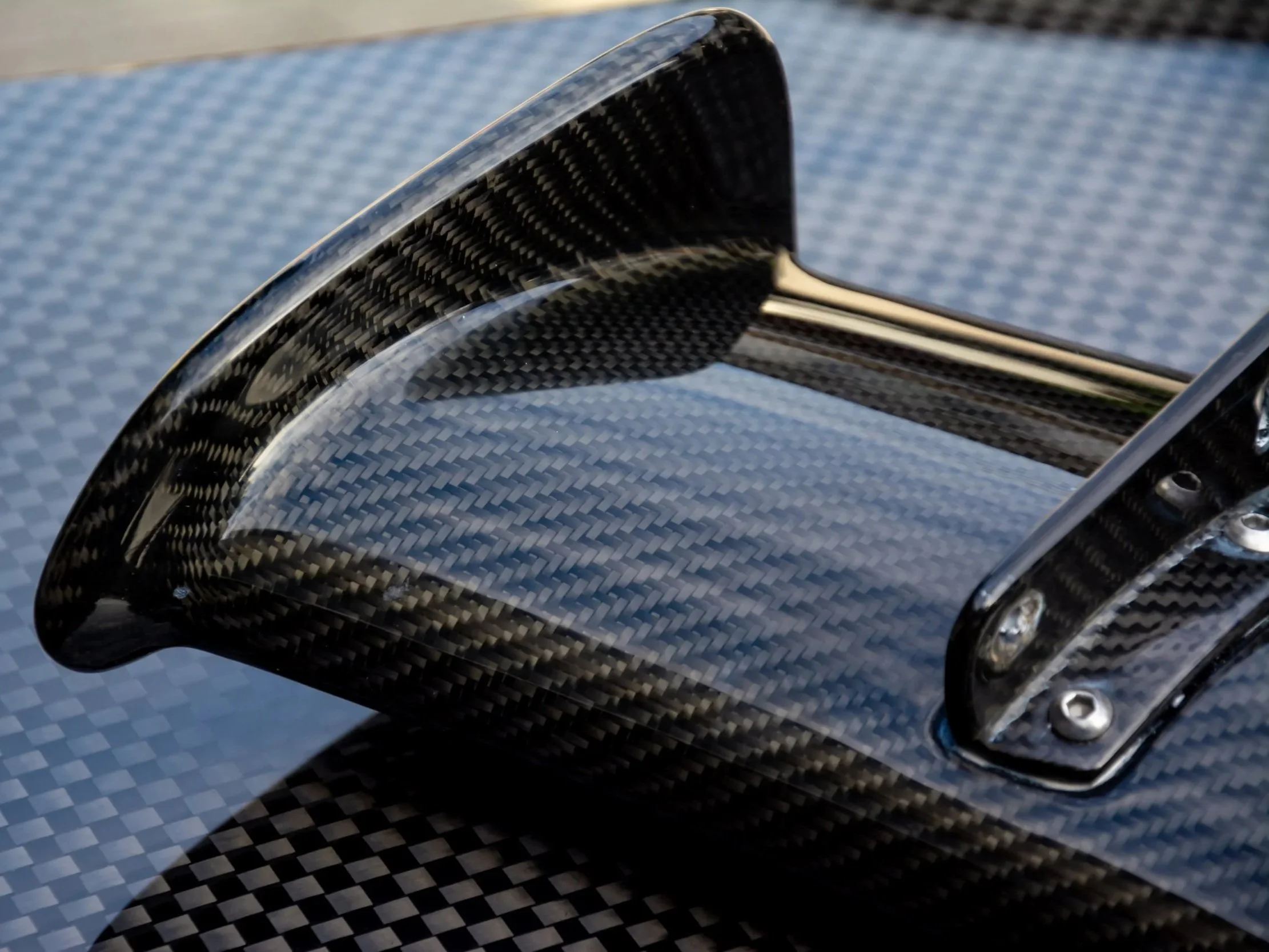 Close-up of a mesh carbon fiber pattern on a vehicle part with metallic bolts.