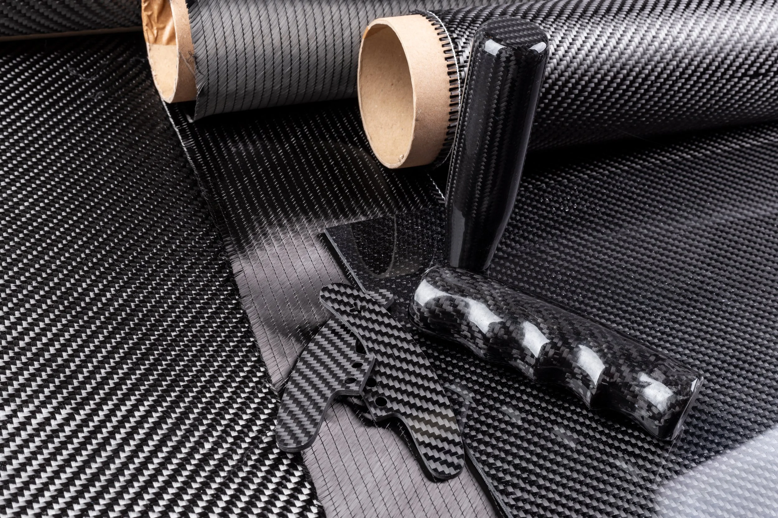 A variety of black carbon fiber vinyl wraps, a roll of adhesive film, and a black carbon fiber interior panel sample with a carbon fiber pattern.