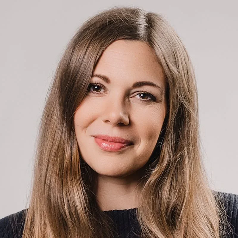 Portrett av en kvinne med langt, brunt hår og smil, iført svart genser
