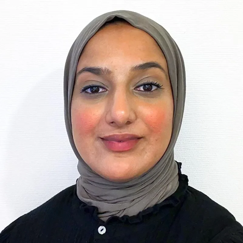 Portrett av en kvinne med hijab som smiler mot kamera, hvit bakgrunn.