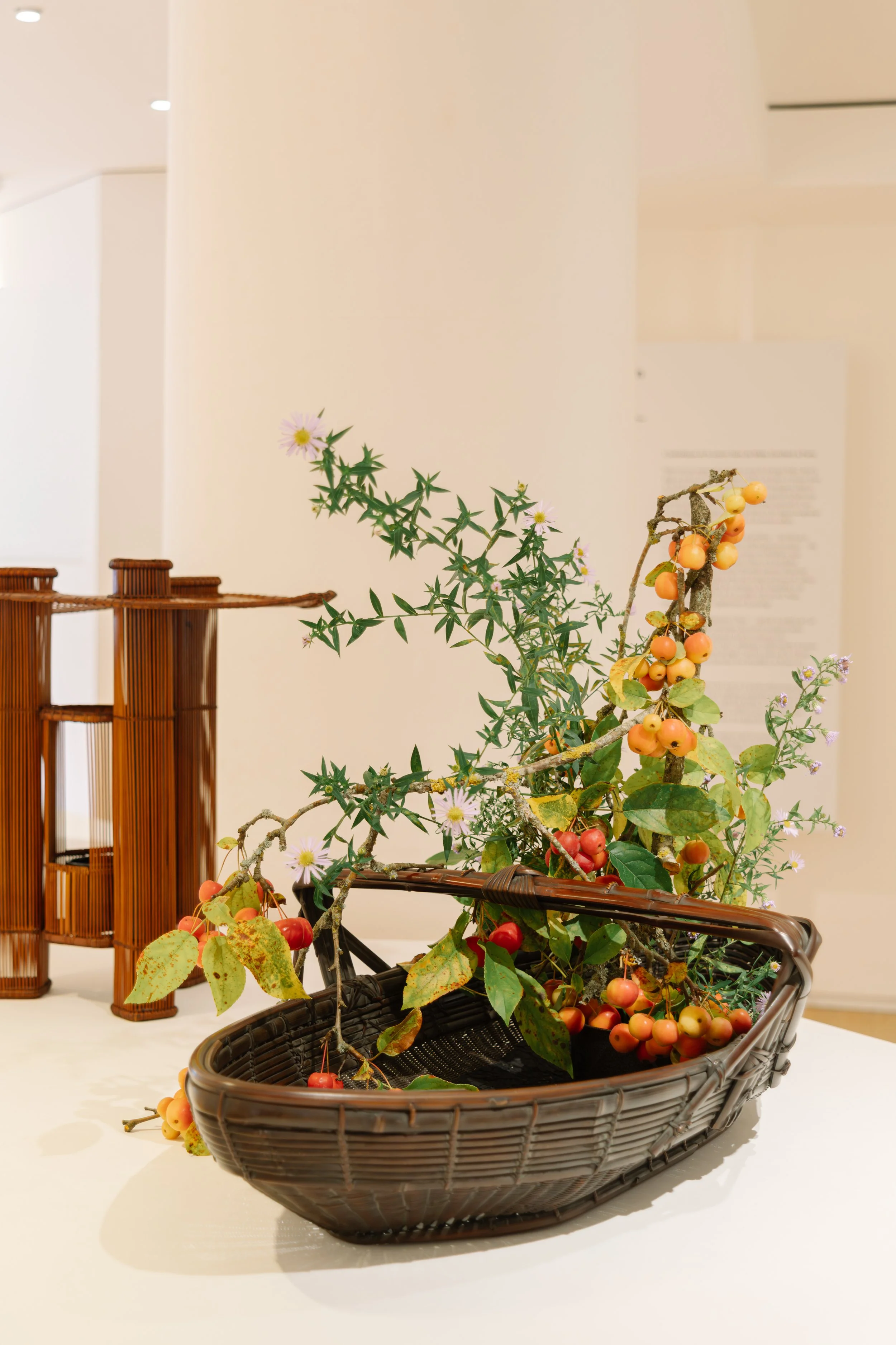 A basket with a branch of orange berries and small pink flowers, indoors with decorative bamboo lanterns in the background.