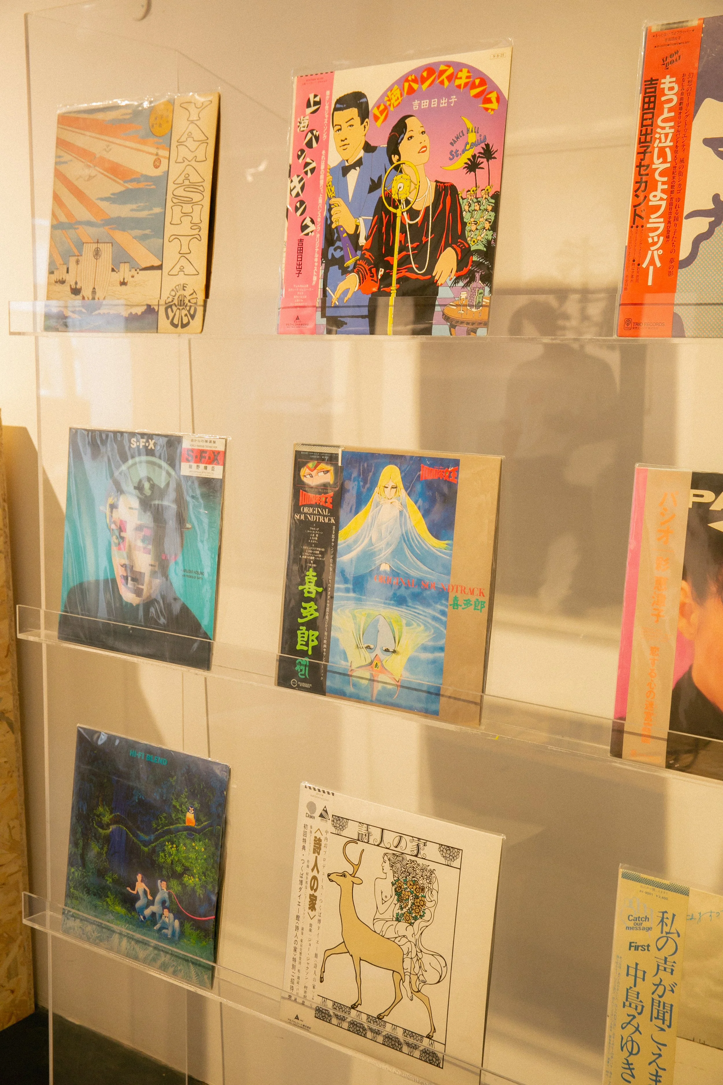 Collection of vintage Japanese illustrated book covers featuring colorful artwork of people and scenes displayed on transparent shelves.