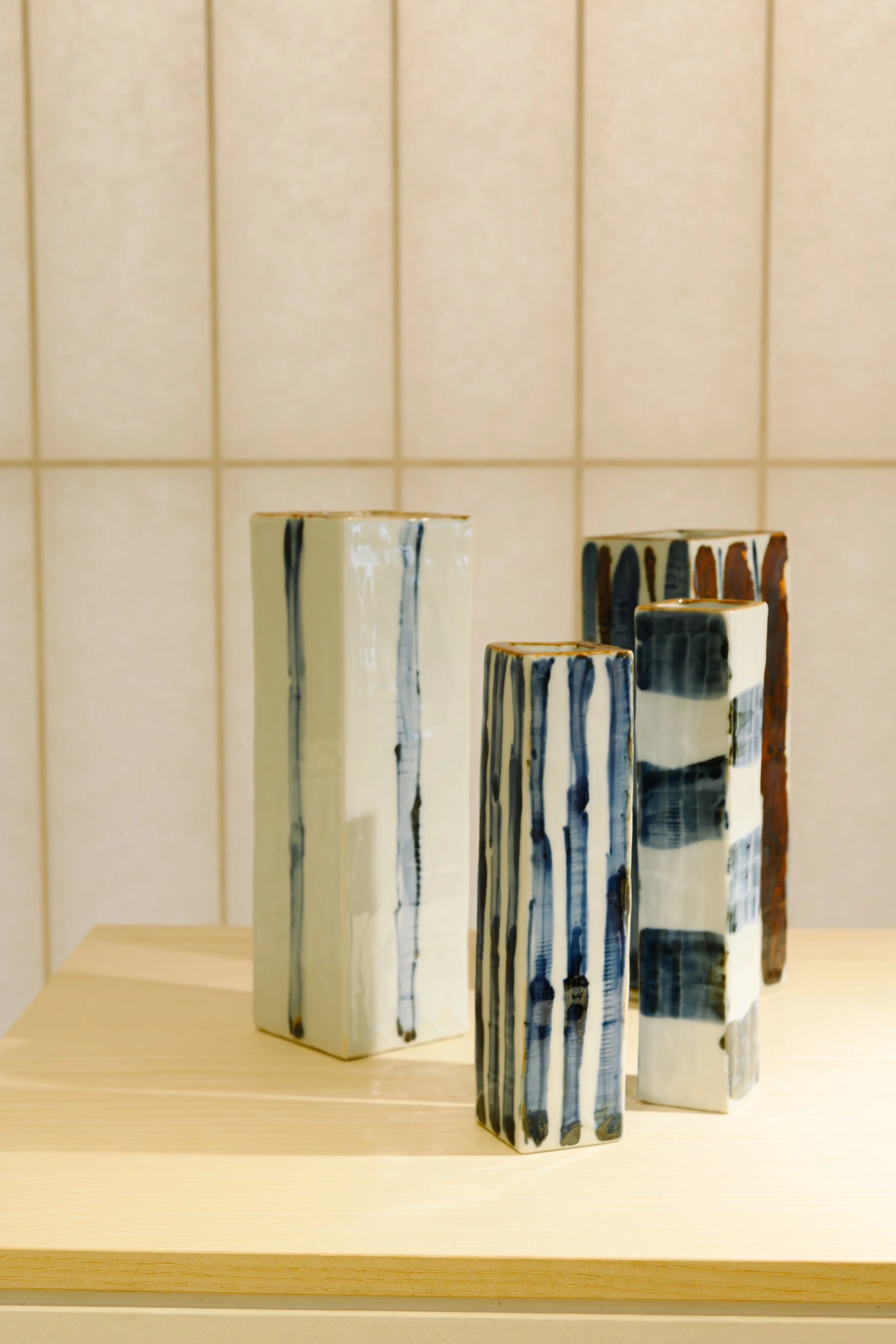 Set of rectangular ceramic vases with black, white, and brown glaze drips, displayed on a wooden surface against a beige tiled wall.