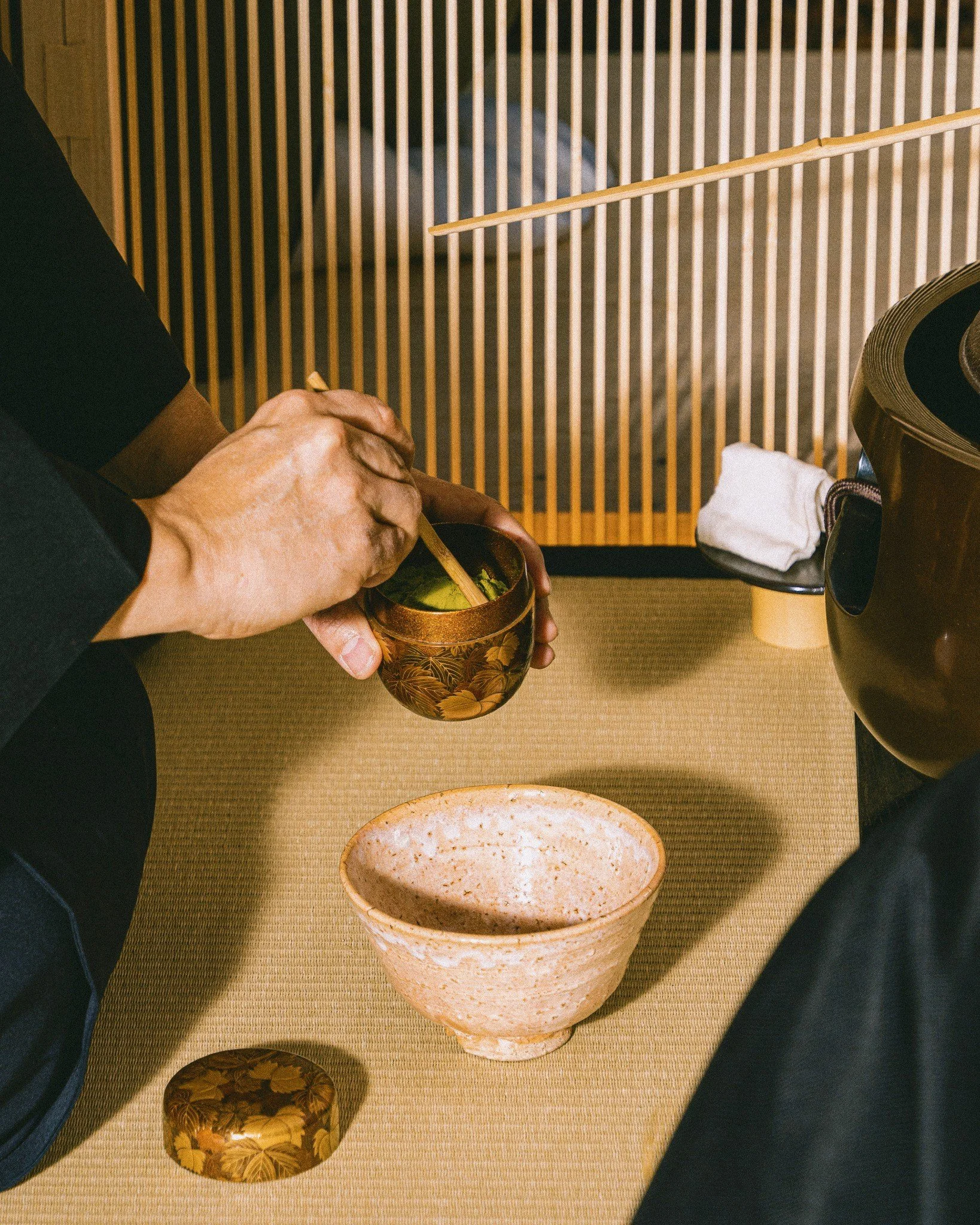 Two people holding hands over a wooden table, with a bowl of green leaf salad, a white oval dish, and a black cup on a beige tablecloth. A rolling pin and a fabric piece are also visible.