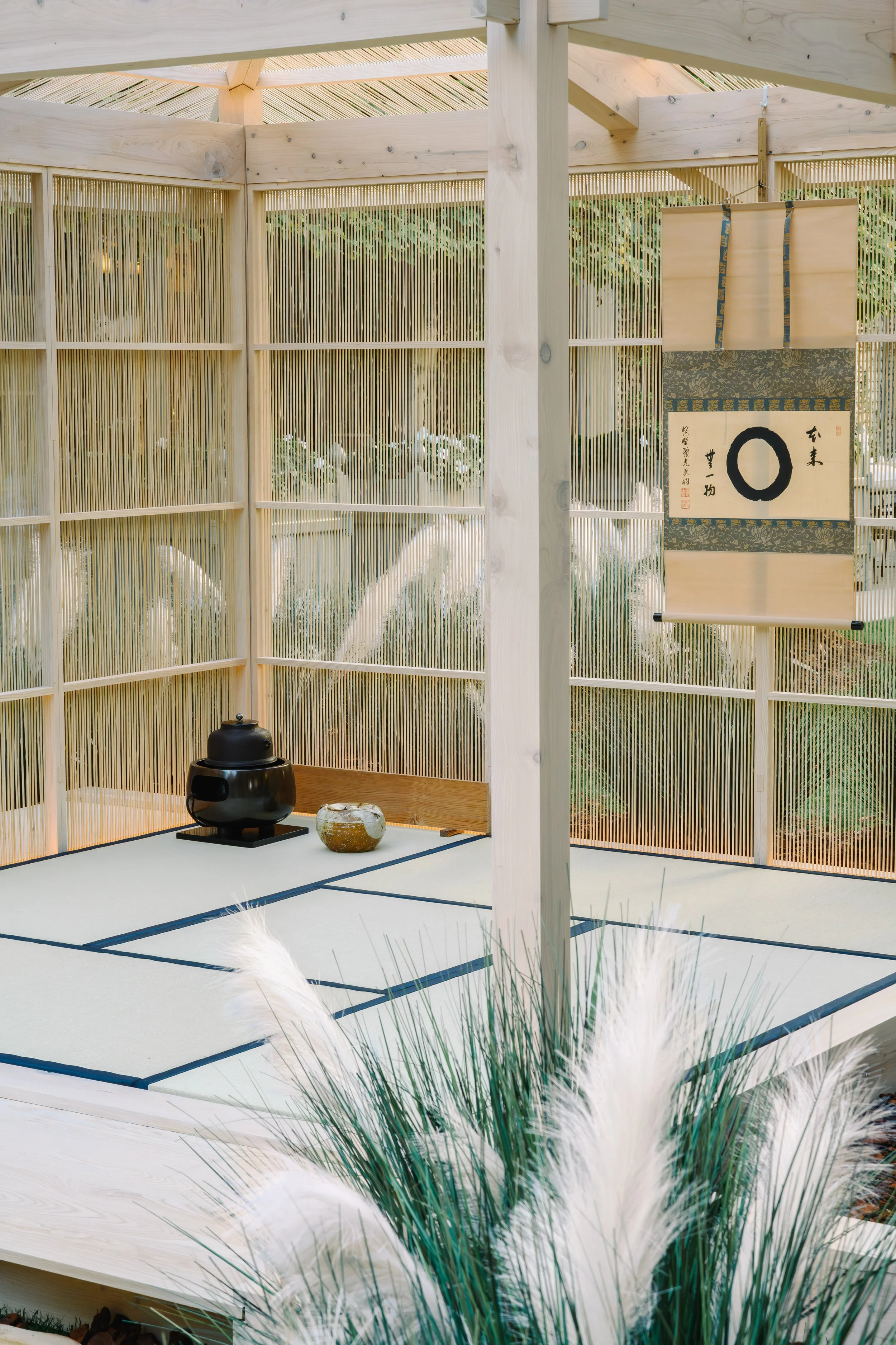 A traditional Japanese tea ceremony scene with a tatami mat and black tea pot, set against a backdrop of wooden screens and decorative folds.