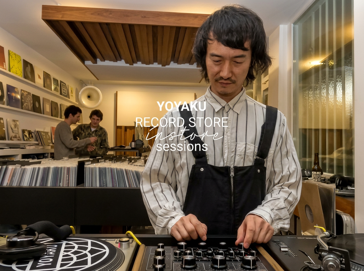 A man with black hair and a striped shirt operating audio equipment in a record store with vinyl albums on display, two people browsing records in the background, and large windows showing a sunset outside.
