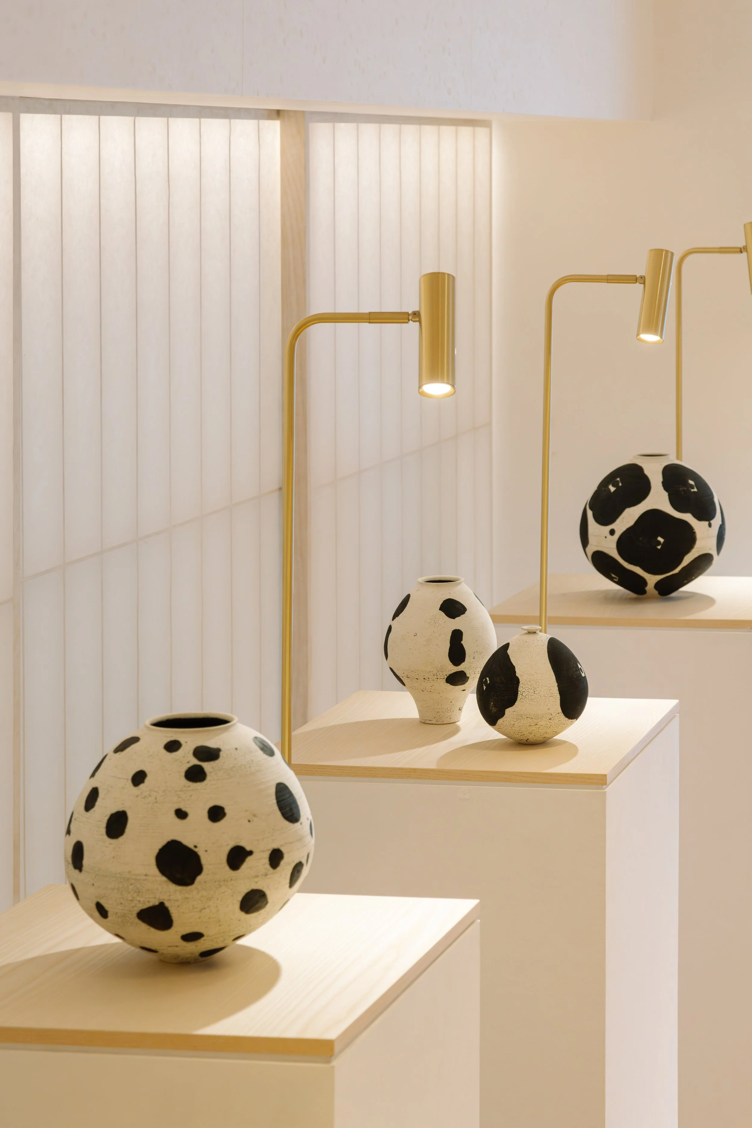 Display of black and white ceramic vases with polka-dot patterns arranged on wooden shelves with brass lamps in the background.