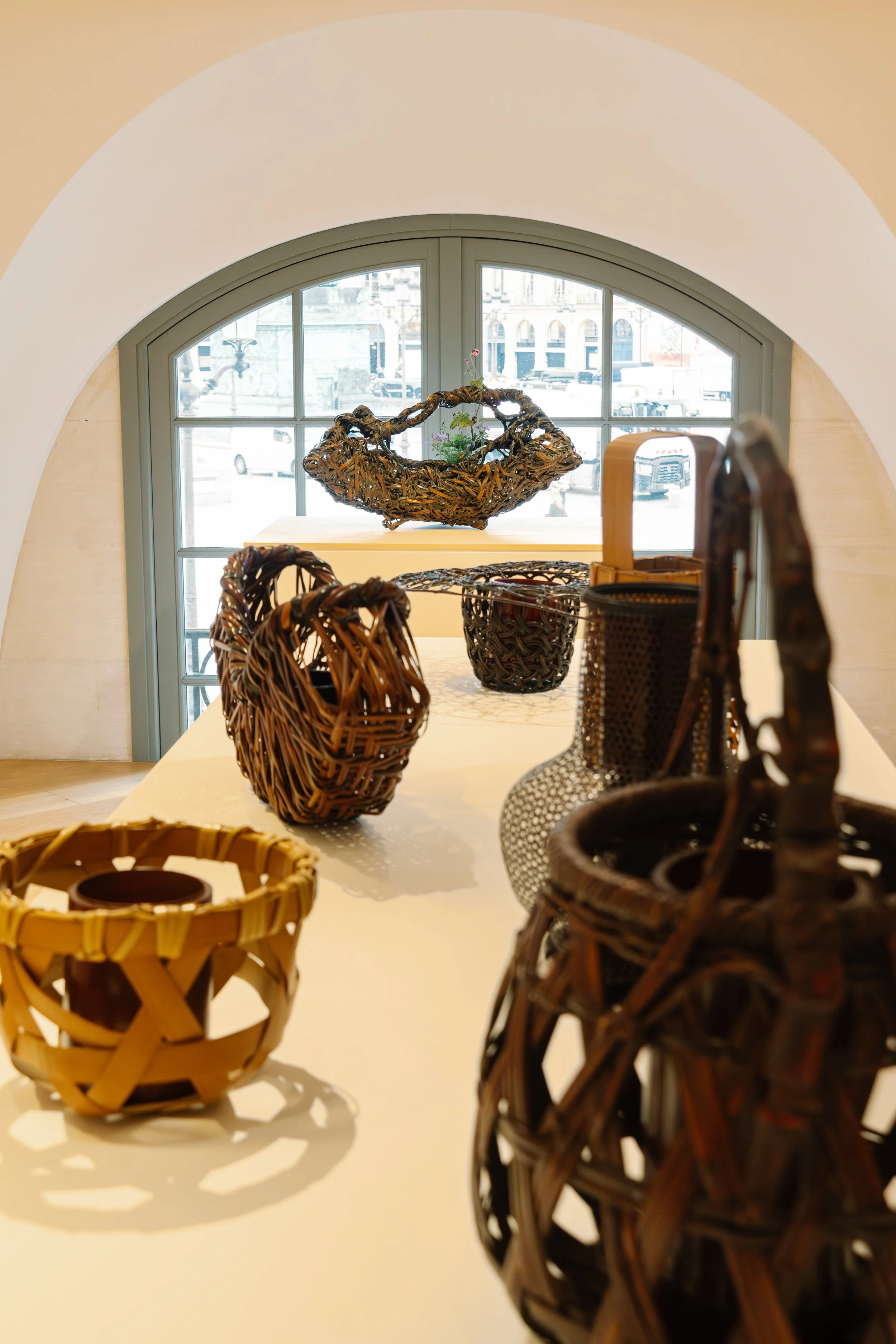 Various wicker baskets and containers placed on a white table in front of a window with a city street visible outside.