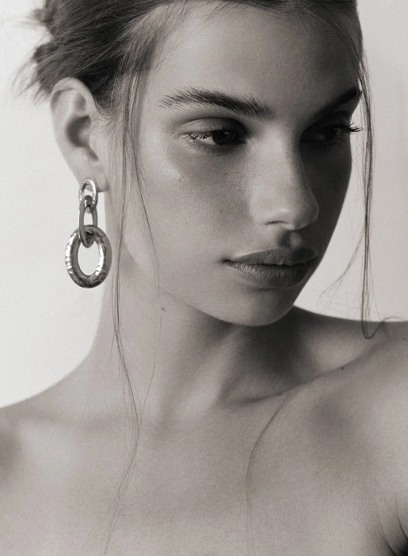 Portrait en noir et blanc d'une femme avec de longs cheveux, portant une boucle d'oreille en métal, regardant légèrement vers la droite.
