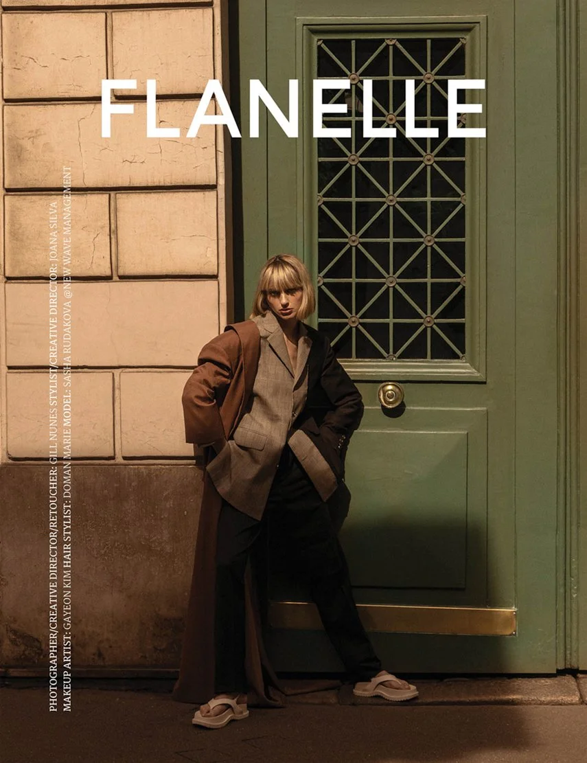 Une femme posant devant une porte verte. Elle porte un manteau long et une veste en demi-tone, avec des baskets, dans un cadre urbain nocturne, avec du texte en gras 'FLANELLE' en haut.