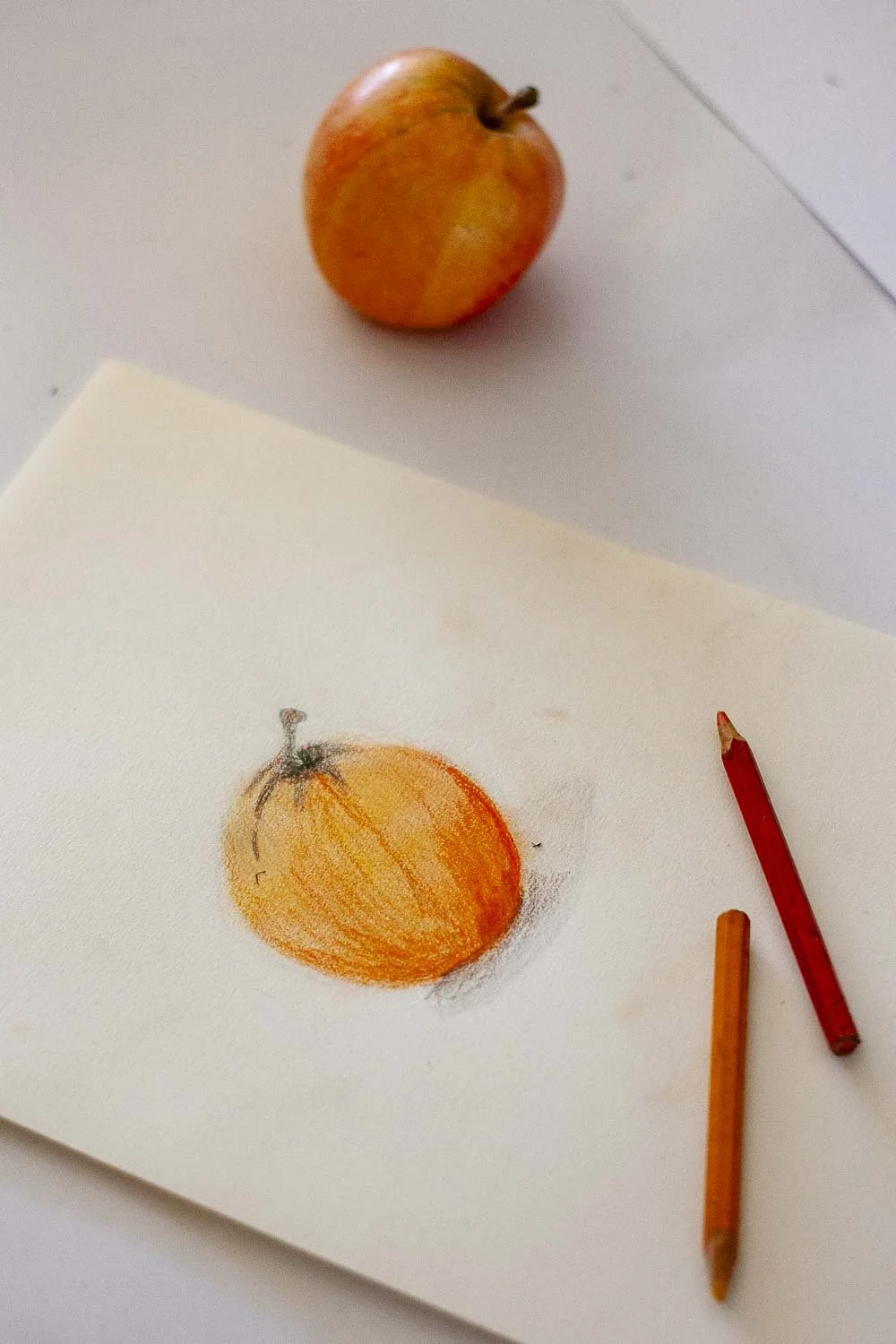 Une pomme réelle et un dessin de pomme réalisé avec des crayons de couleur sur une feuille de papier.