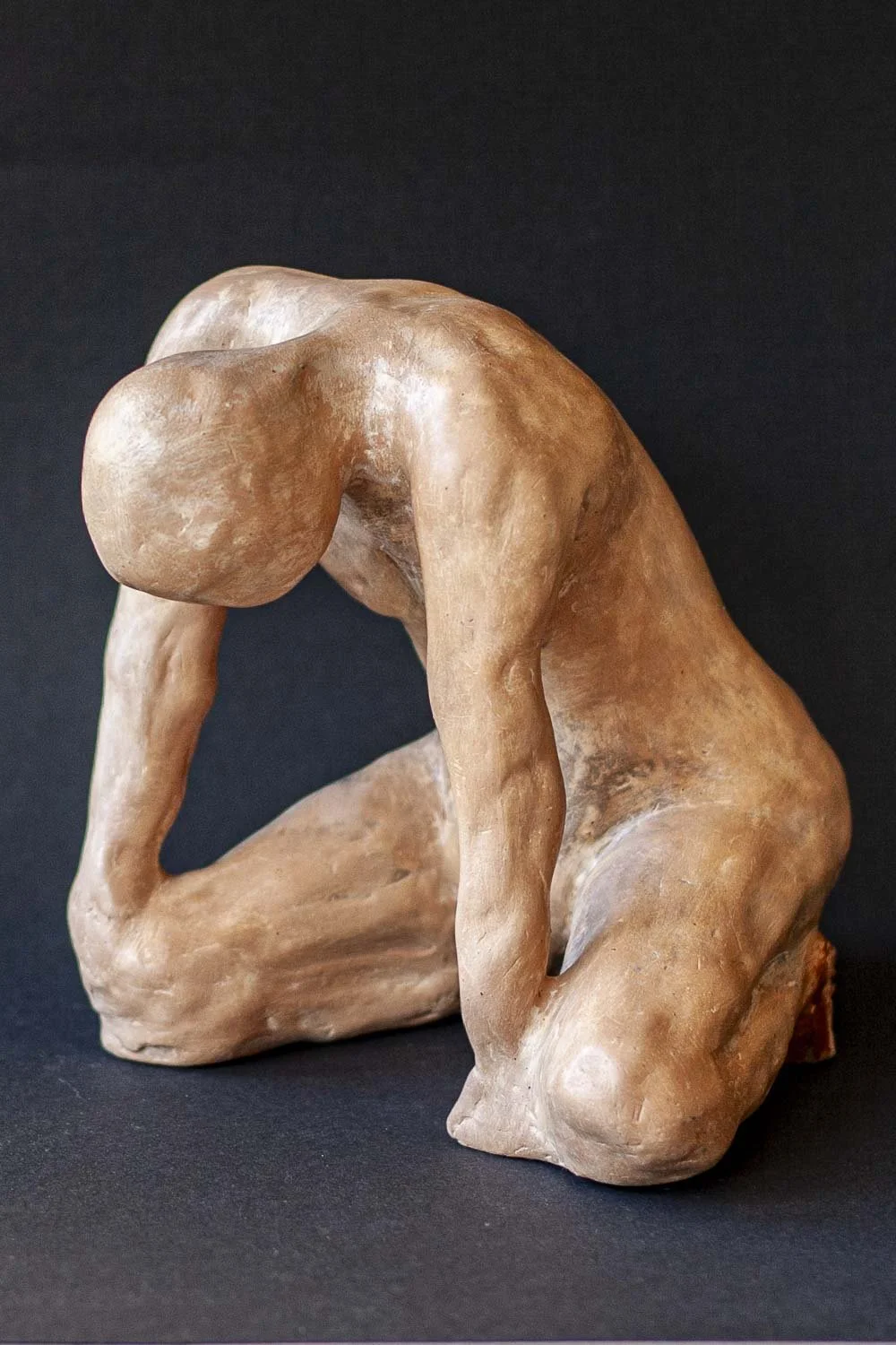 Sculpture en argile représentant un homme agenouillé avec la tête baissée et les mains posées sur ses jambes