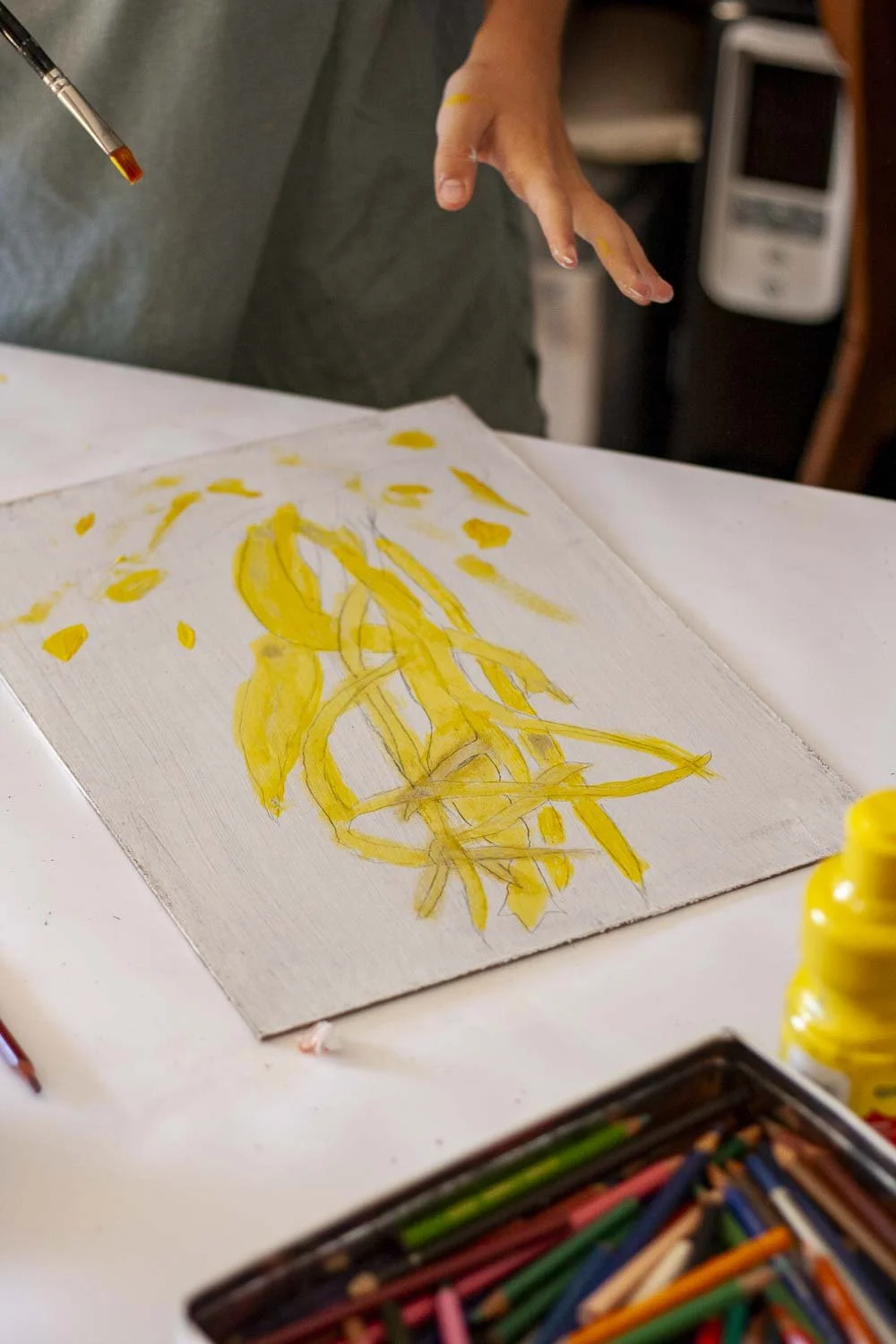 Une personne utilise un pinceau pour peindre une toile avec une image abstraite jaune. Il y a un étui à crayons de couleur, une bouteille de peinture jaune et une perception d'un système de chaleur en arrière-plan.