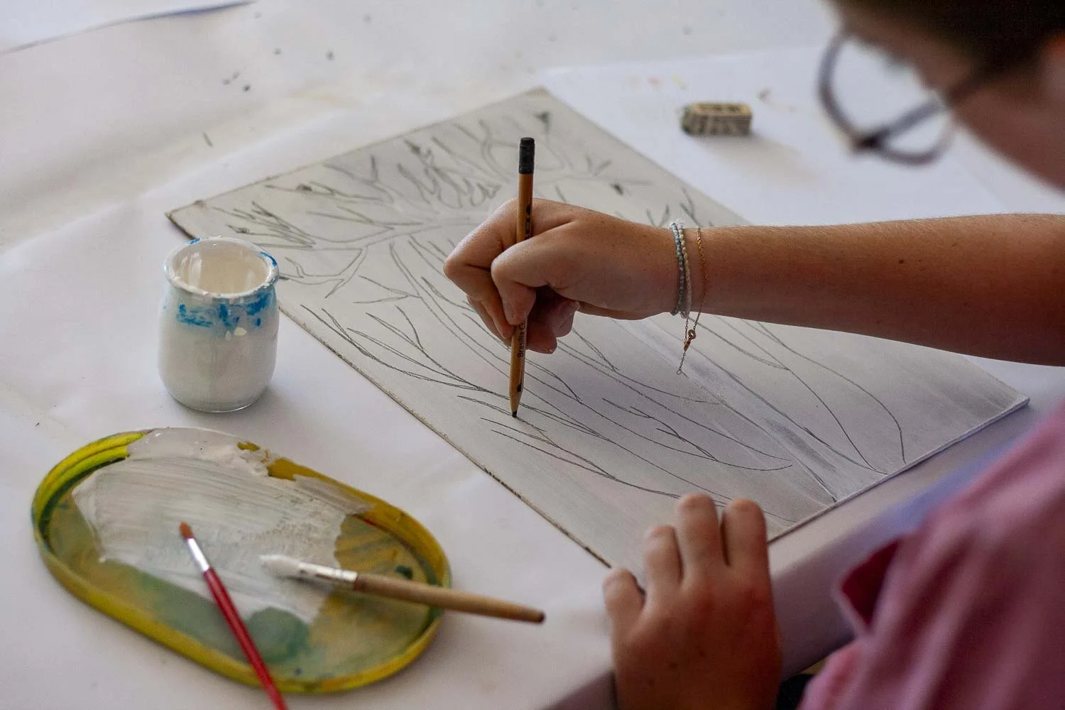 Une personne en train de dessiner une nature morte avec un pinceau sur une feuille blanche, entourée de peinture et d'une palette.