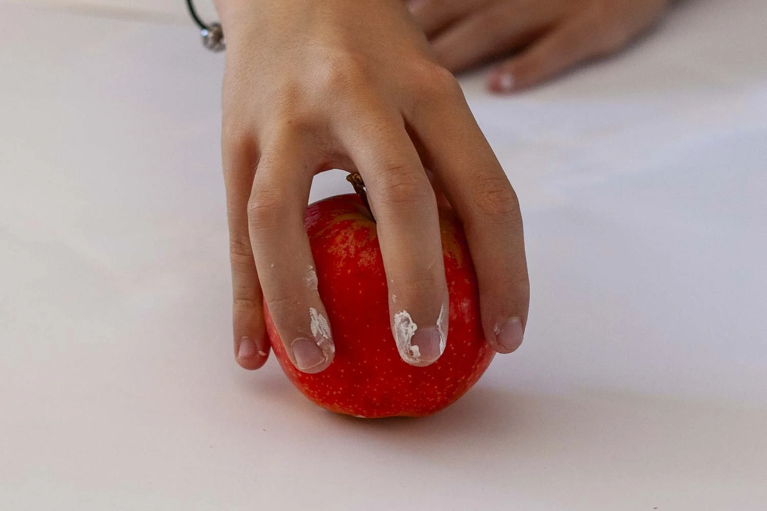 Une main qui tient une pomme rouge sur une surface blanche