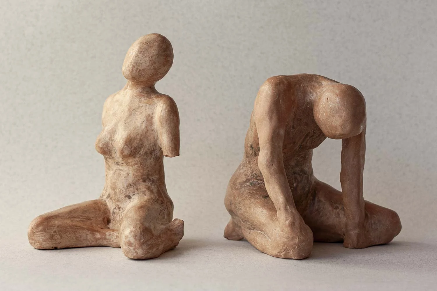 Deux sculptures en argile représentant deux êtres humains, l'une à genoux avec les bras derrière le dos et l'autre à genoux avec la tête baissée.