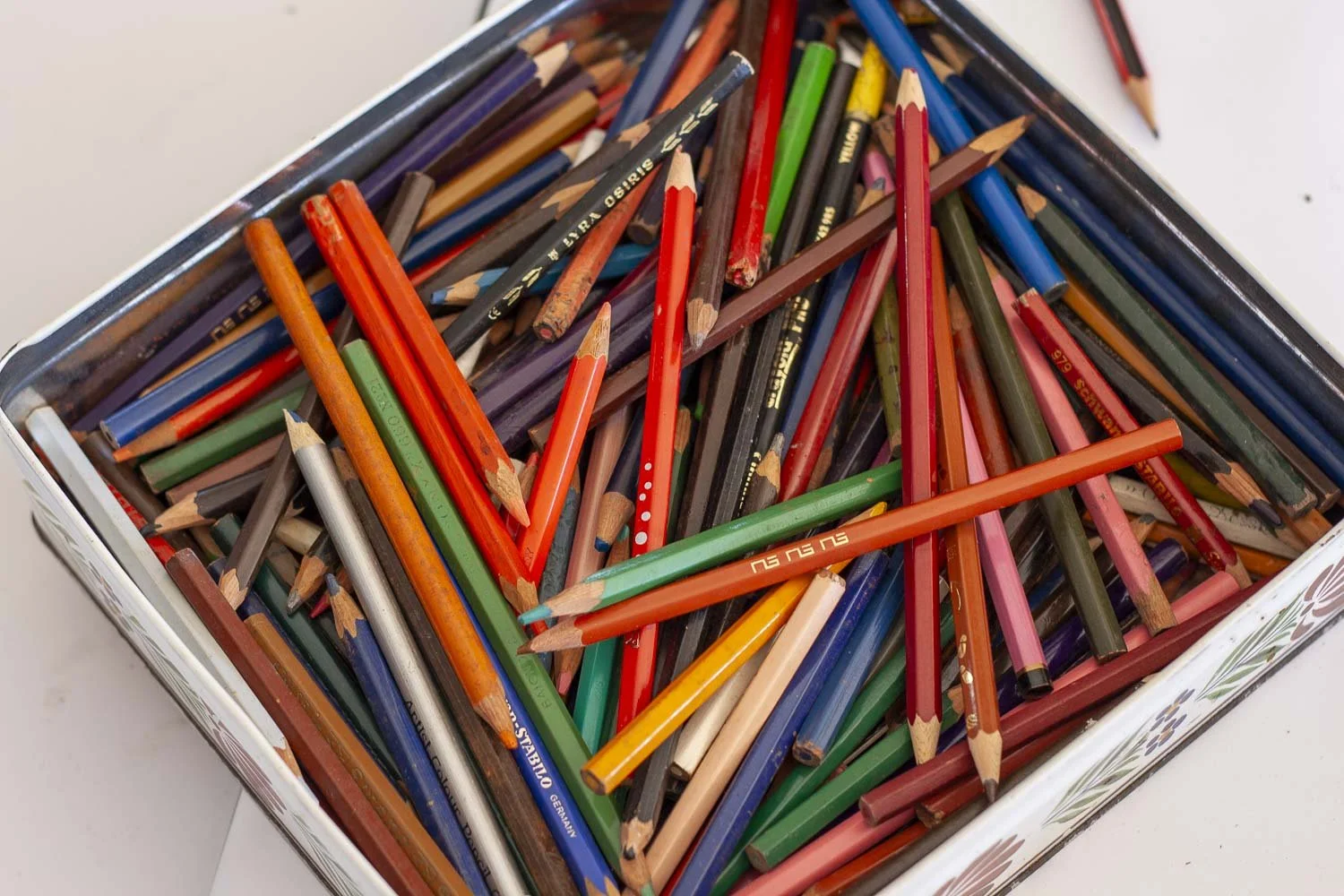 Une boîte en métal contenant des crayons de couleur usés et cassés disposés de manière désordonnée.