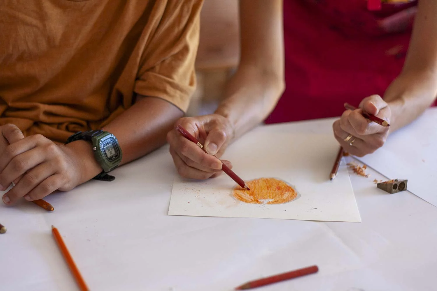 Deux personnes regardant un dessin au crayon coloré orange sur une feuille blanche, assises à une table.