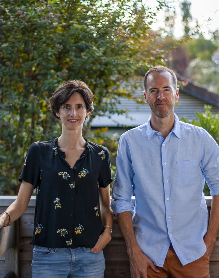Un homme et une femme posent ensemble à l'extérieur sur une terrasse en bois, avec des arbres en arrière-plan