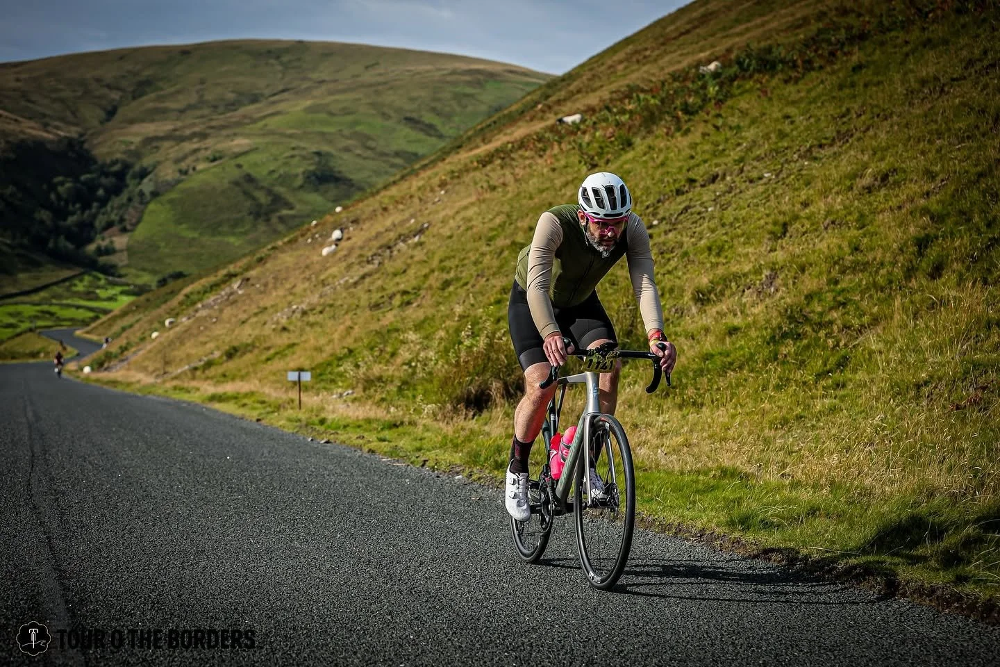 A cyclist riding on a mountain road with green hills on both sides during daytime.