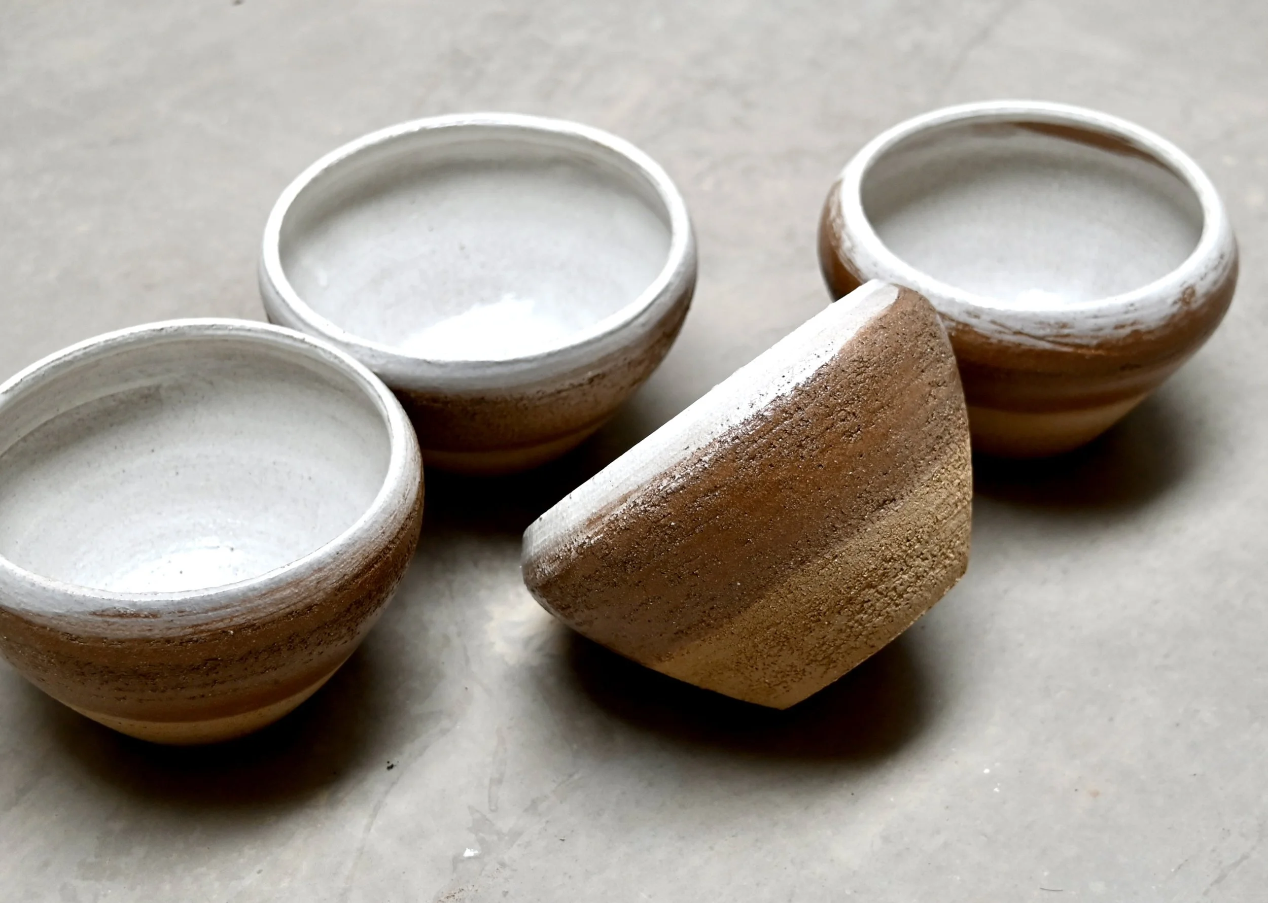Belle image d'un assemblage de bols en grès roux, réalisés par Jeanne Yaa Stenmanns au tournage. Ils sont posés sur une surface grise. 