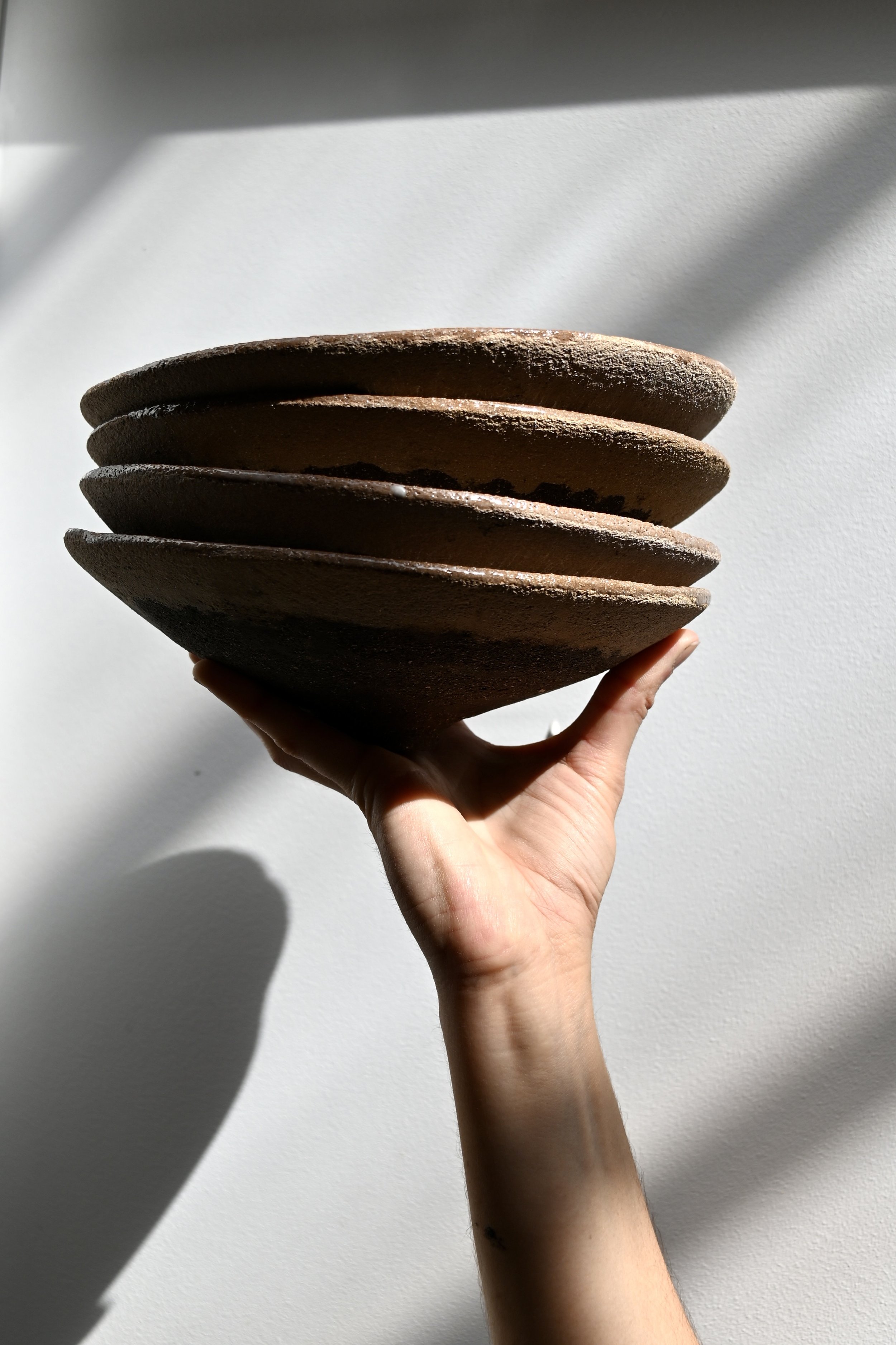Main tenant une pile d'assiettes en grès roux, fond blanc avec ombres naturelles, pièces réalisées au modelage par Jeanne Yaa Stenmanns