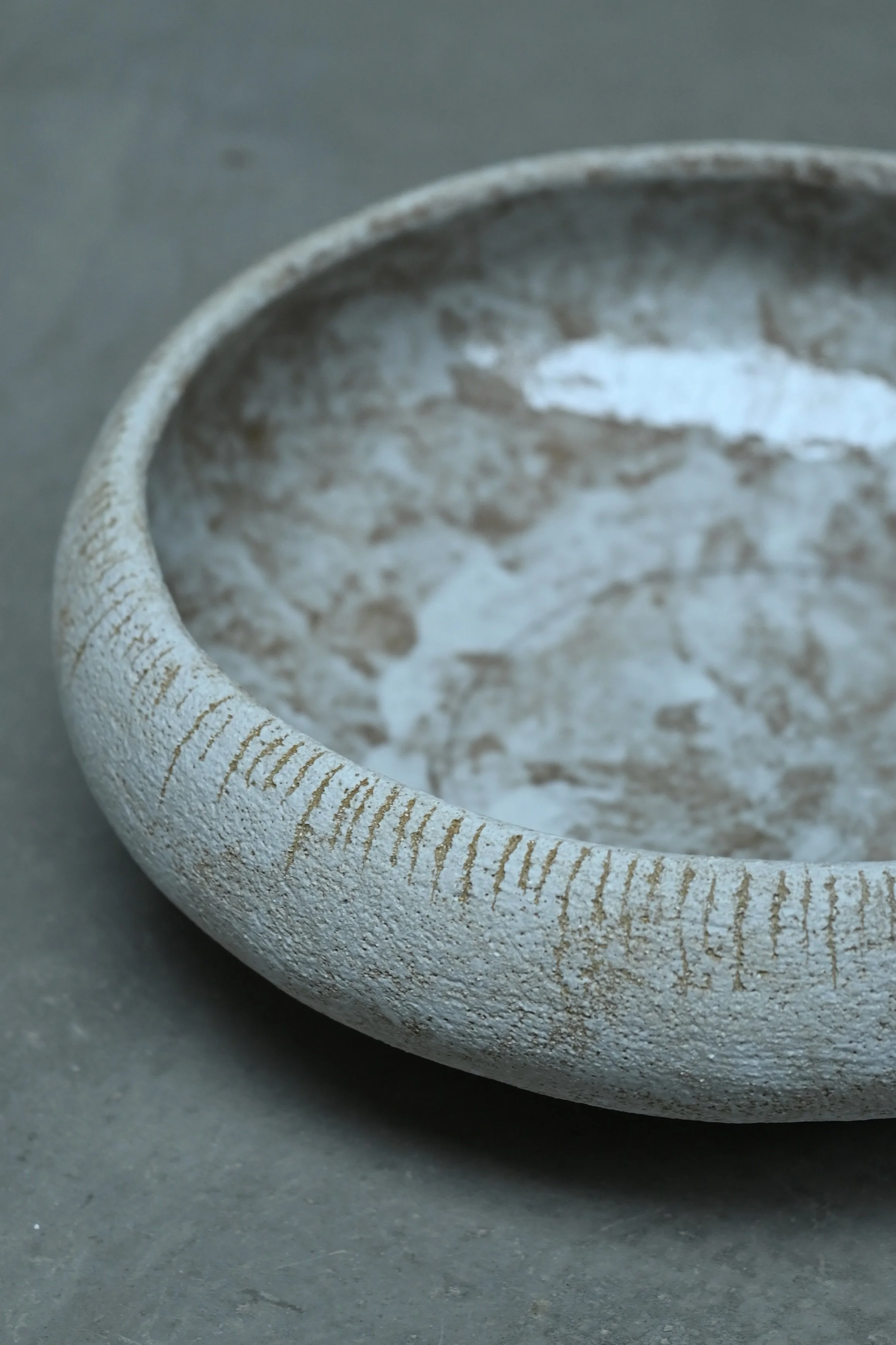 Un grand plat en grès roux et décoré avec de l'engobe blanche, posé sur une surface grise. Le plat est artisanal, avec une décoration simple de lignes gravées autour de ses bords, réalisé au modelage par Jeanne Yaa Stenmanns. 