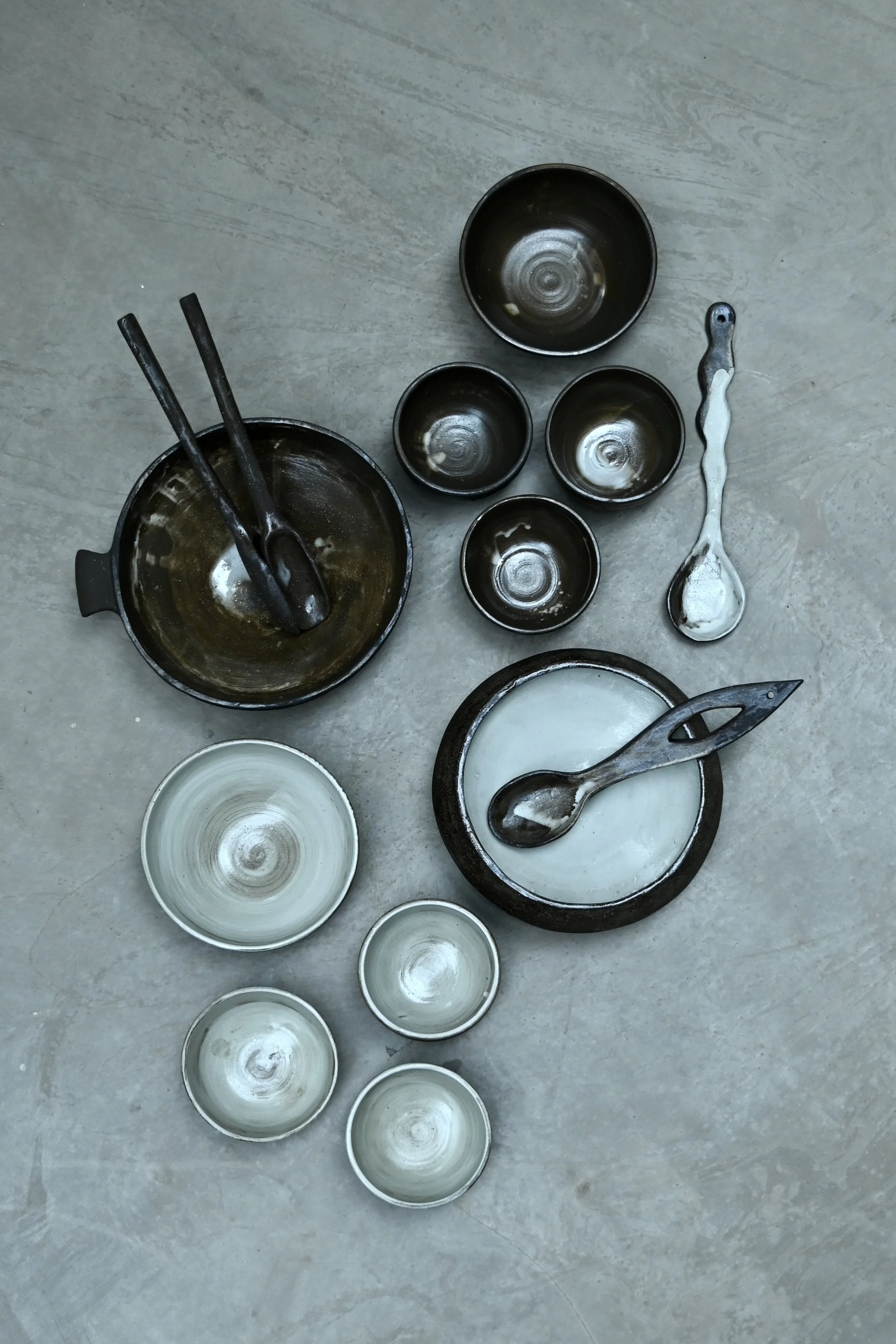 Assortiment de bols et ustensiles de cuisine en céramique ou en métal, certains avec des restes de nourriture ou de pâte, posés sur un sol en pierre ou en béton.