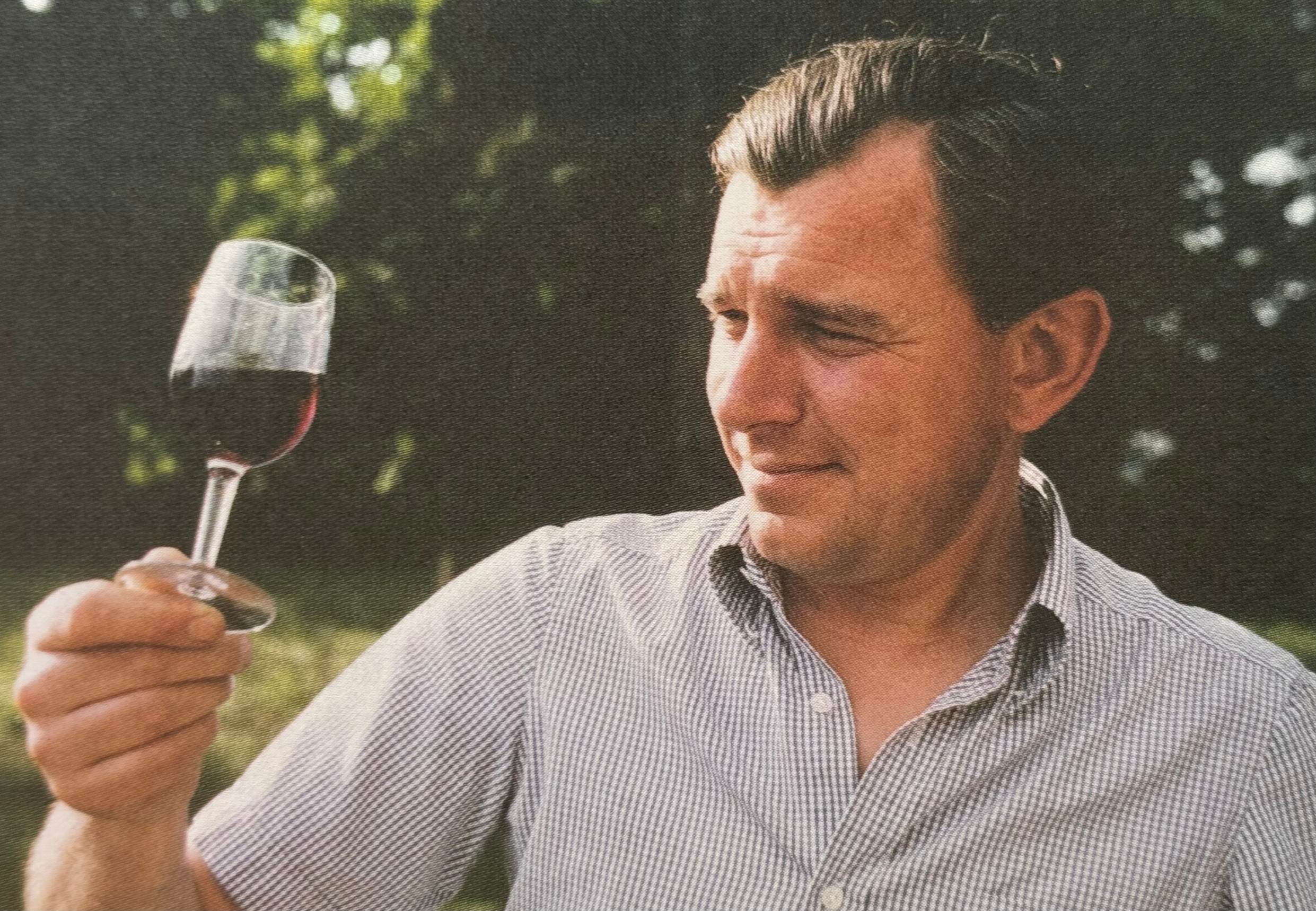 Man in a checkered shirt holding a glass of red wine outdoors.