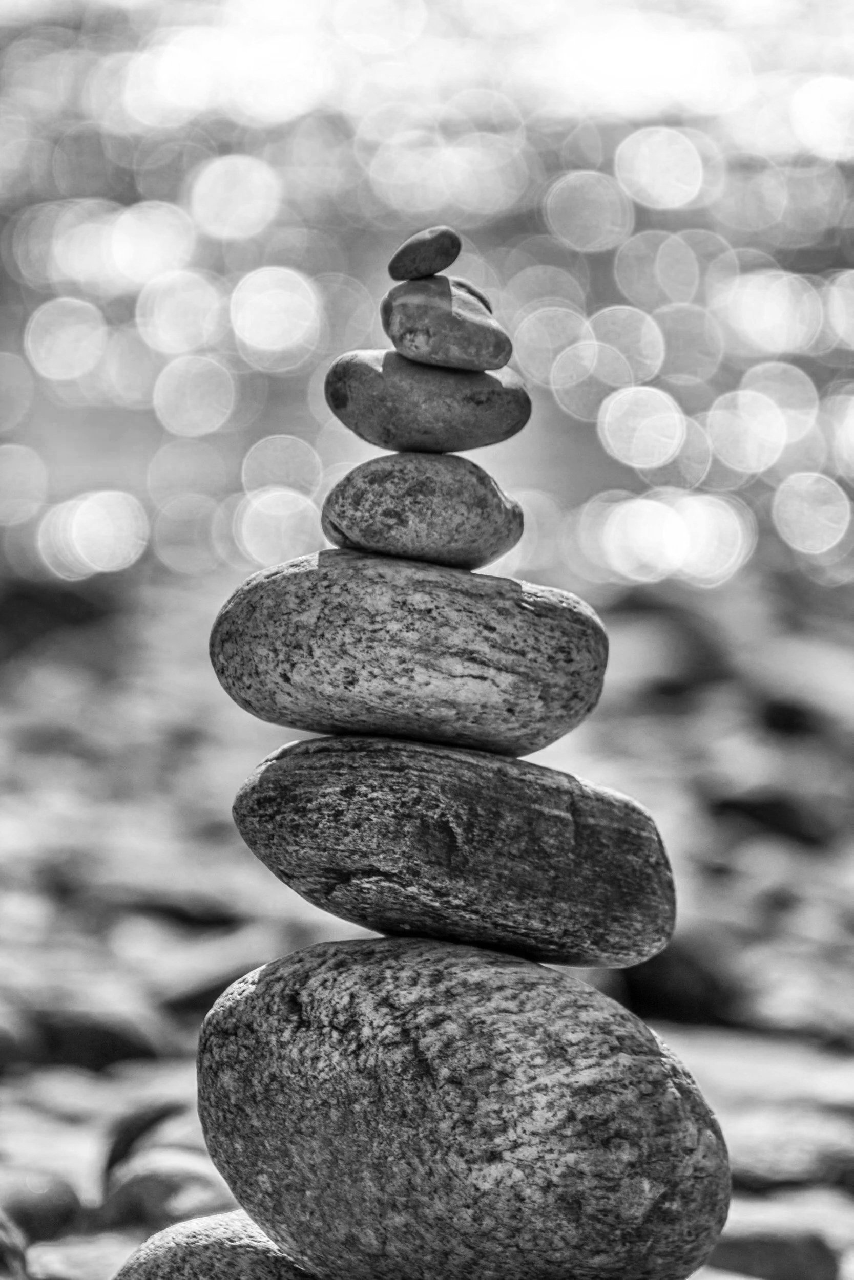 Stacked smooth rocks on a sandy beach with blurred sunlight reflections in the background