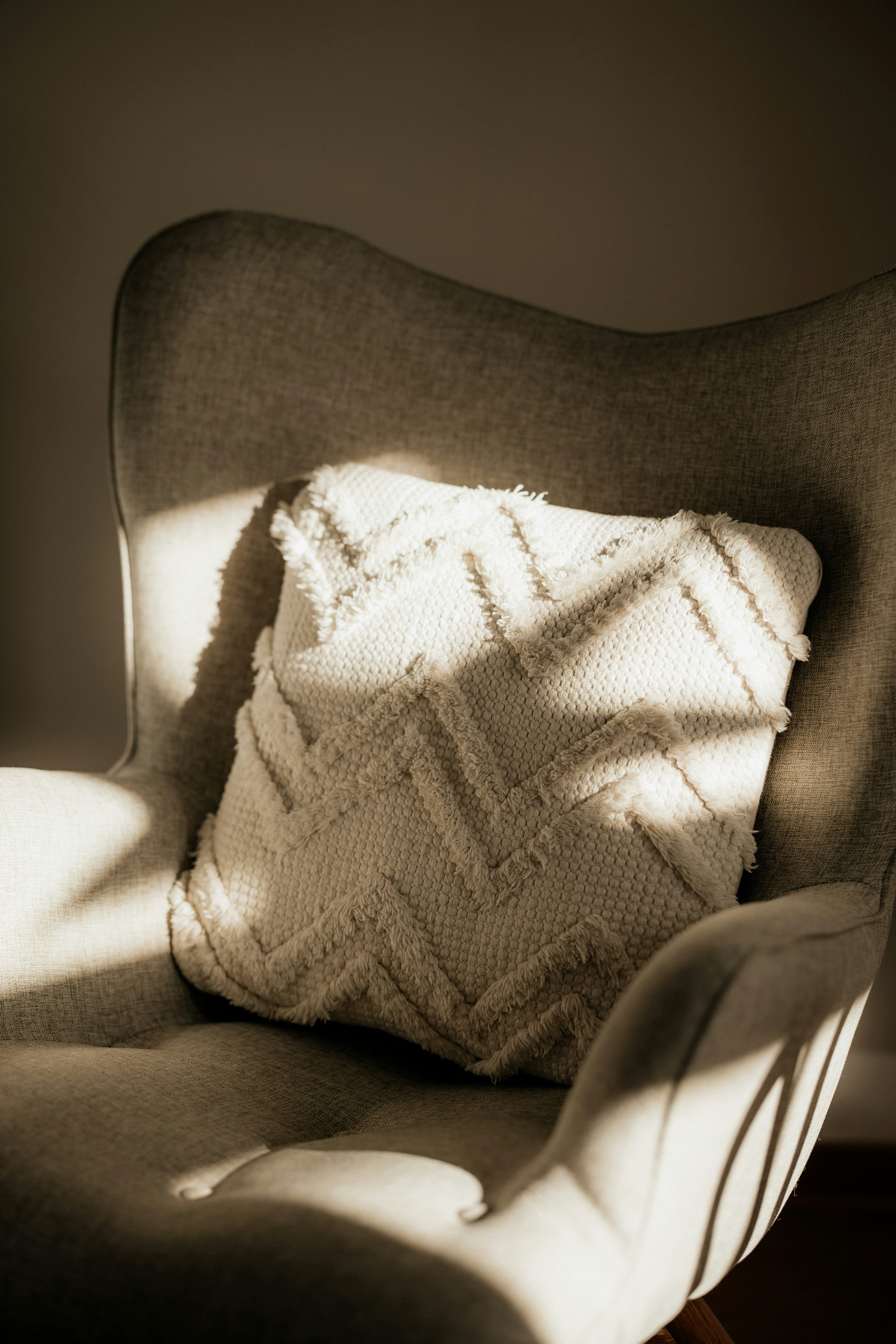 A cozy beige armchair with a textured off-white throw blanket draped over it, illuminated by warm, soft lighting.