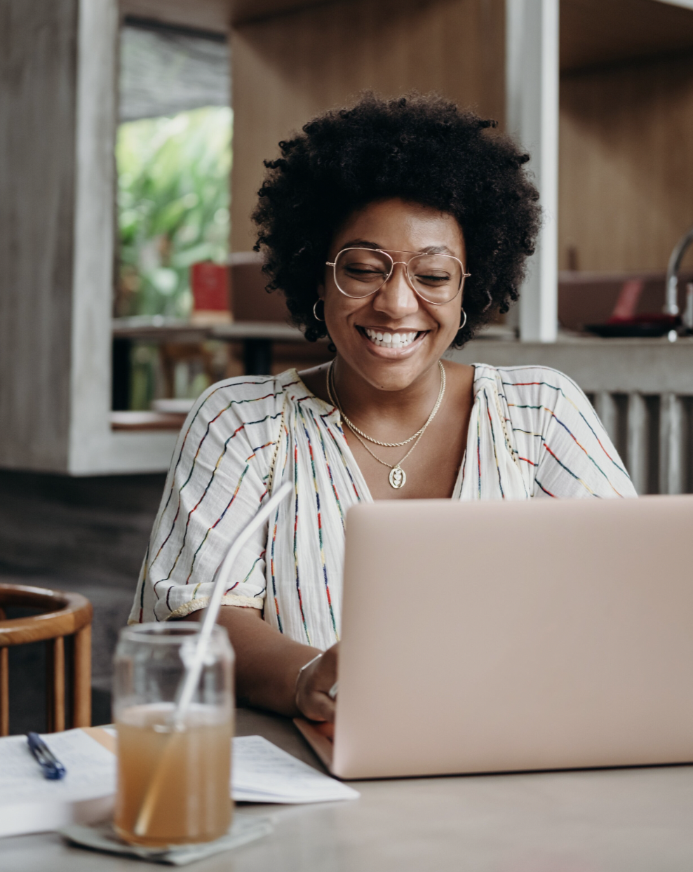 Woman with curly hair and glasses smiling while using a laptop — representing accessible, trauma-informed online therapy and psychological support at REST in Nairobi and London