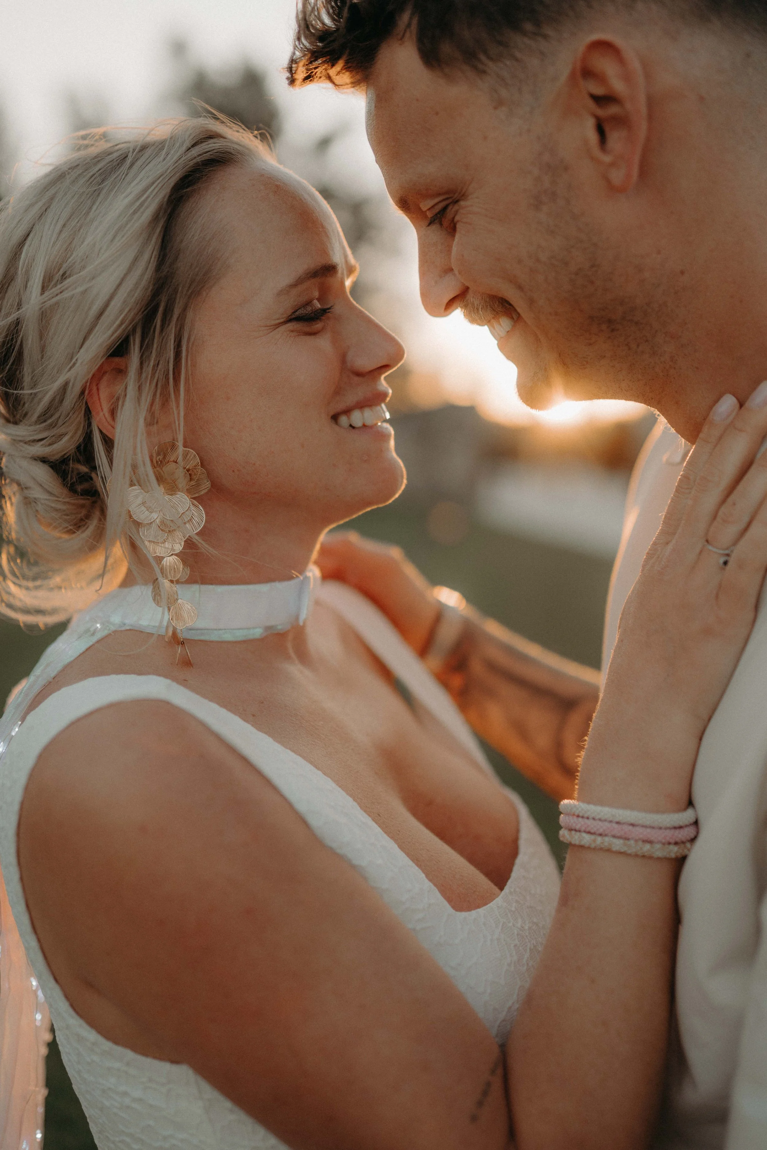 A man and woman smiling and touching foreheads outdoors during sunset.