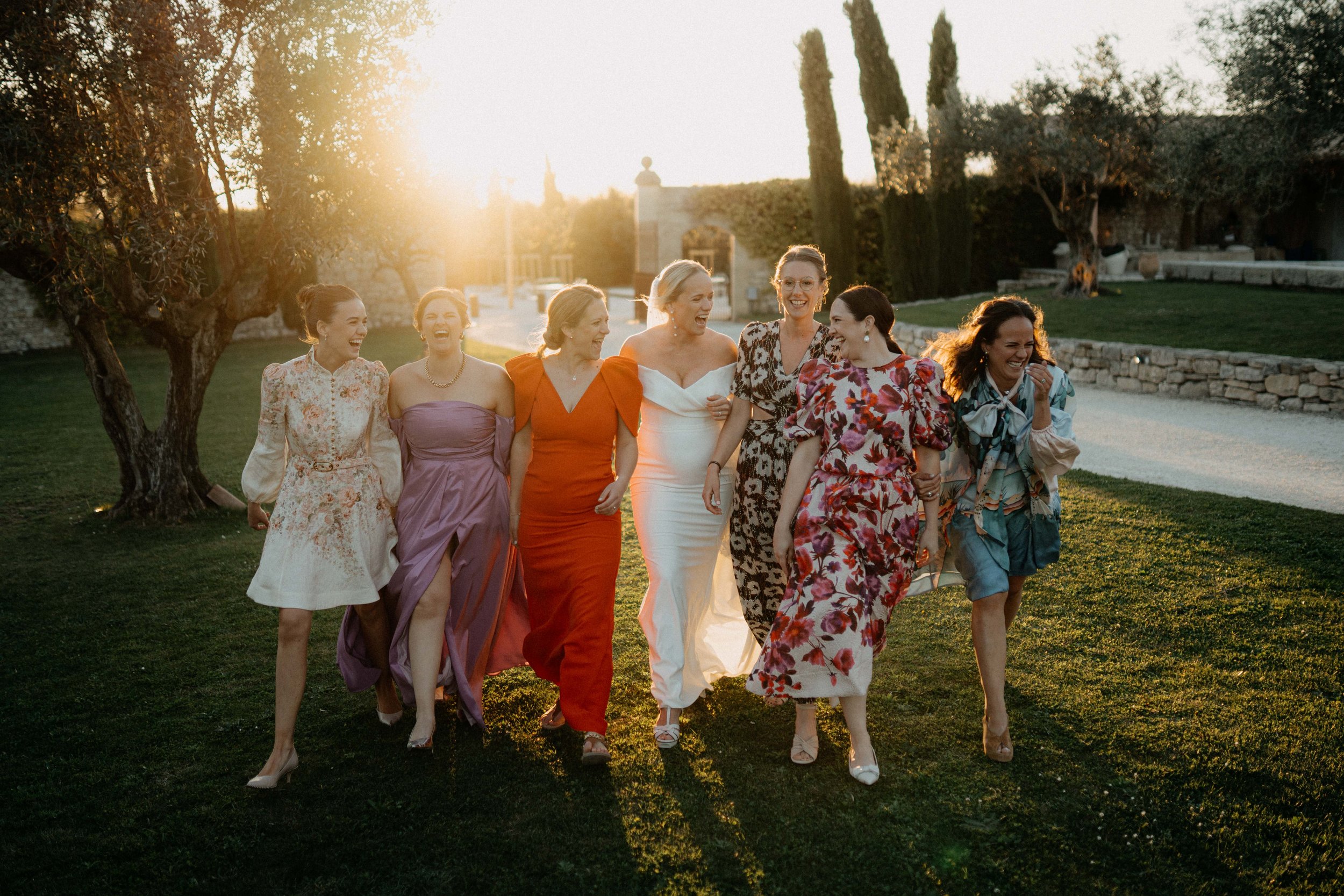 A group of women in colorful dresses walking outdoors at sunset, smiling and laughing.