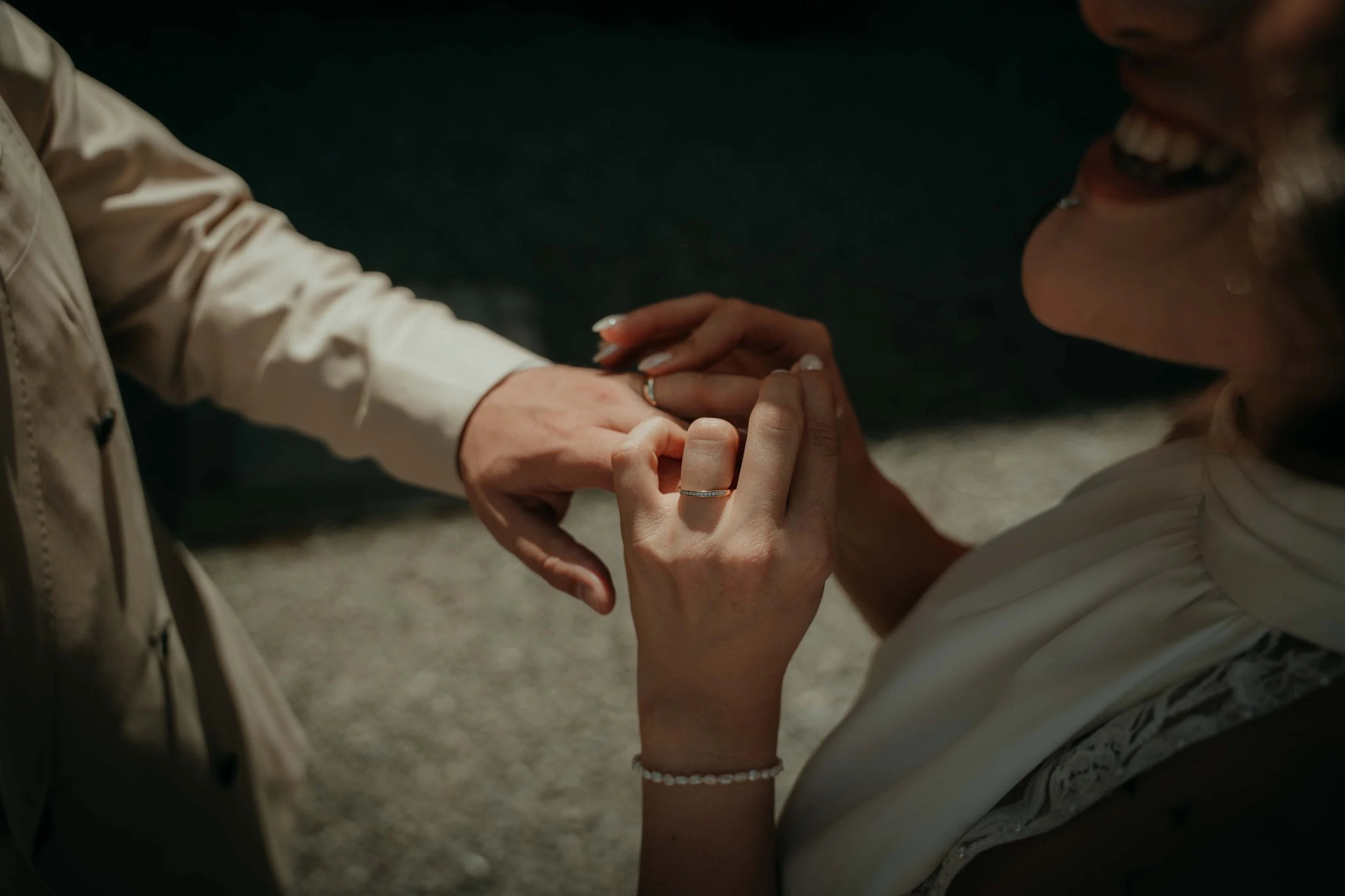 Two people holding hands, with one person gently grasping the other's hand in a caring gesture. The scene appears to be outdoors with a dark background.