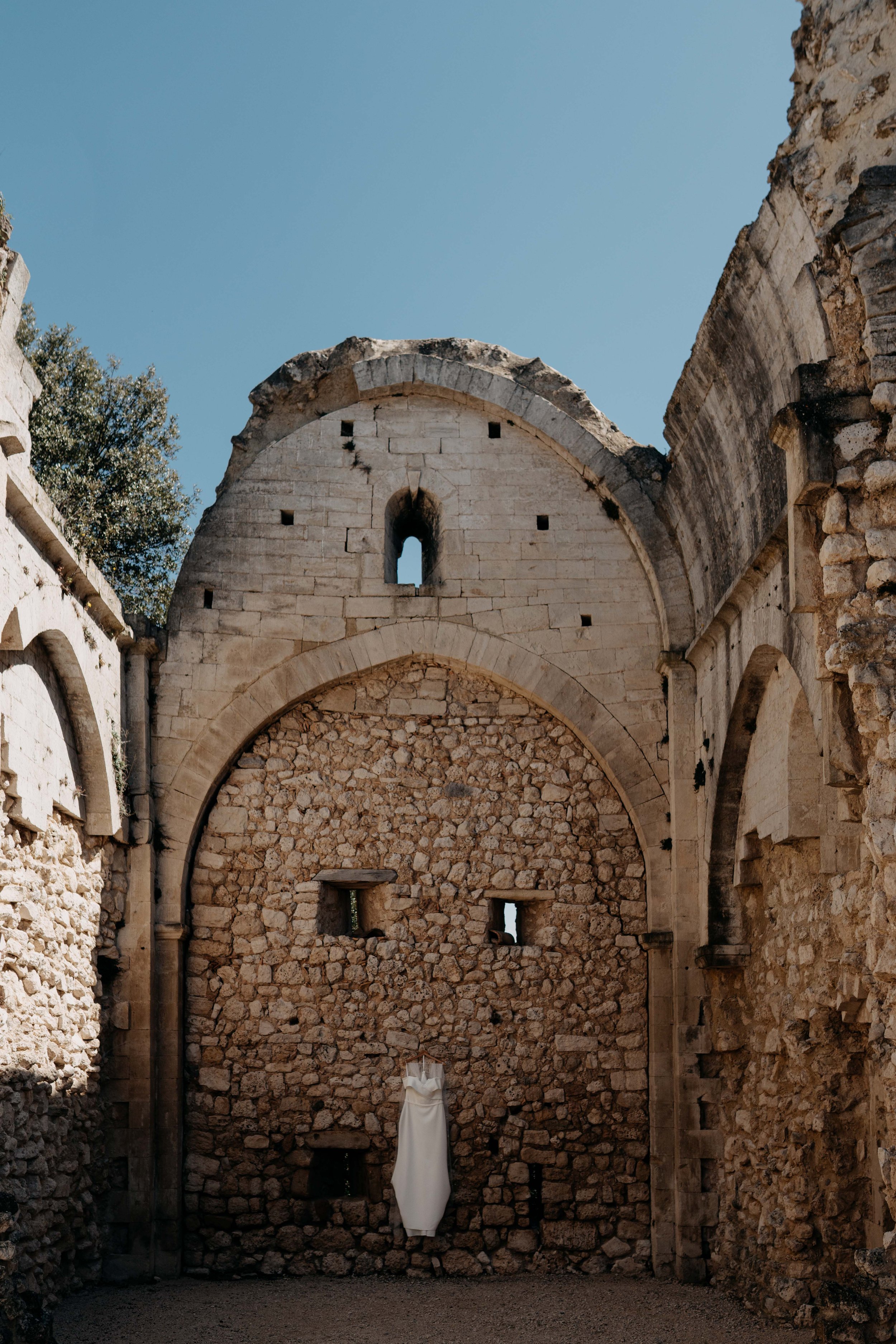 View of ancient stone ruins with an arched window, some small openings, and a white cloth-draped object in a collapsed area, under a clear blue sky.