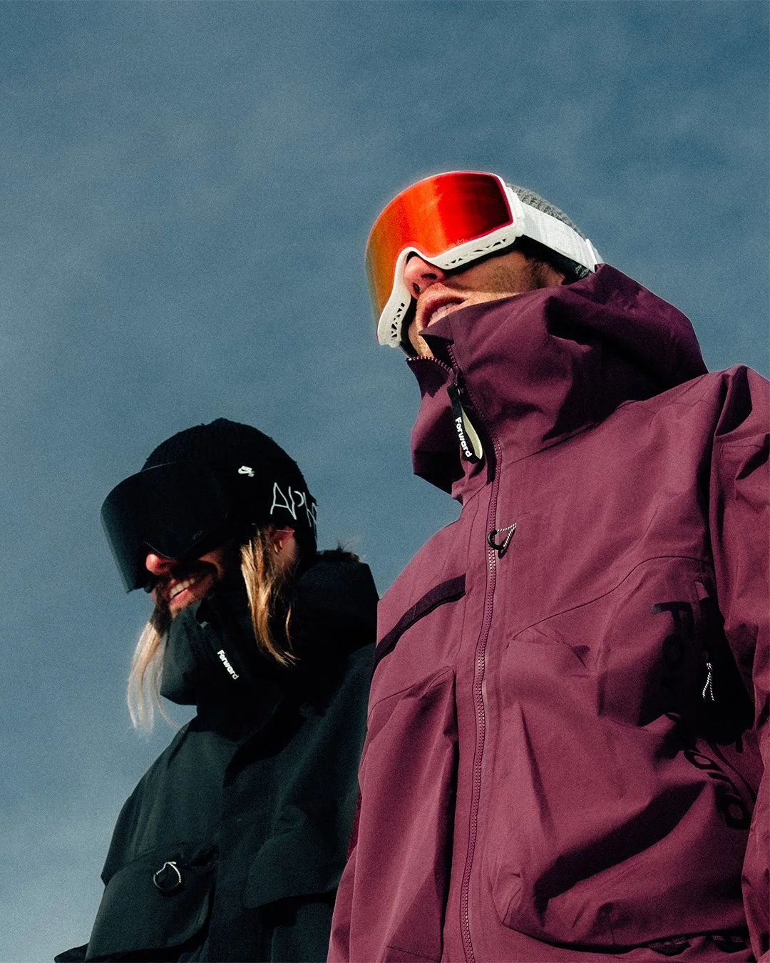 Deux personnes portant des vêtements de ski et des lunettes de protection en outdoor, sous un ciel gris.