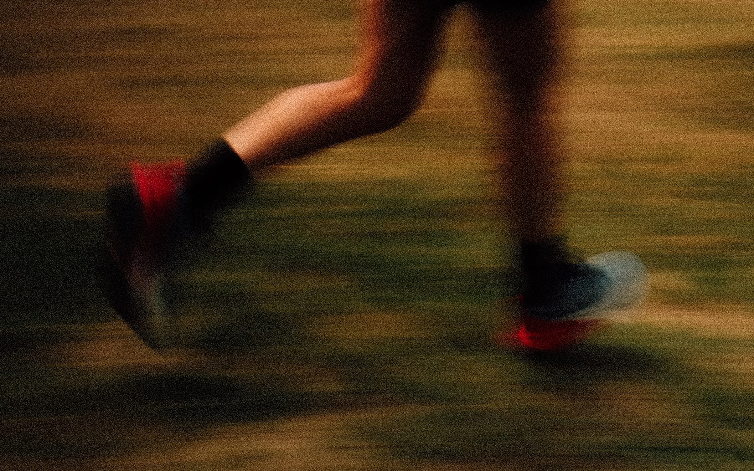 Une personne en mouvement, probablement en train de faire du sport ou une activité physique, avec un fond flou et une tenue sombre avec des touches de rouge.