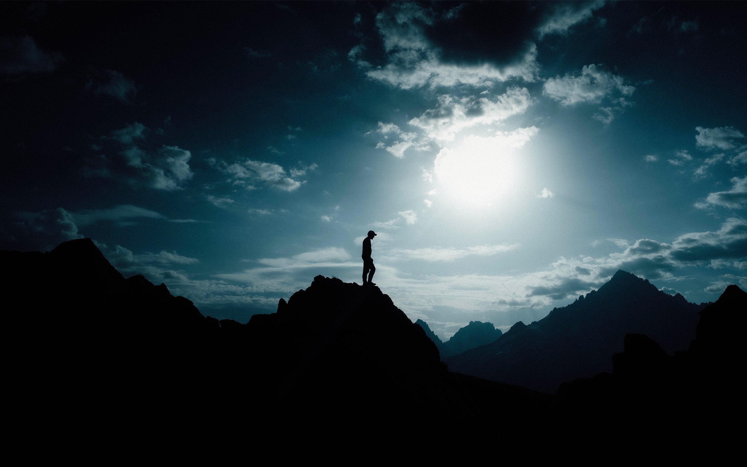 Silhouette d'une personne debout sur une montagne avec un ciel nuageux et un soleil brillant en arrière-plan.