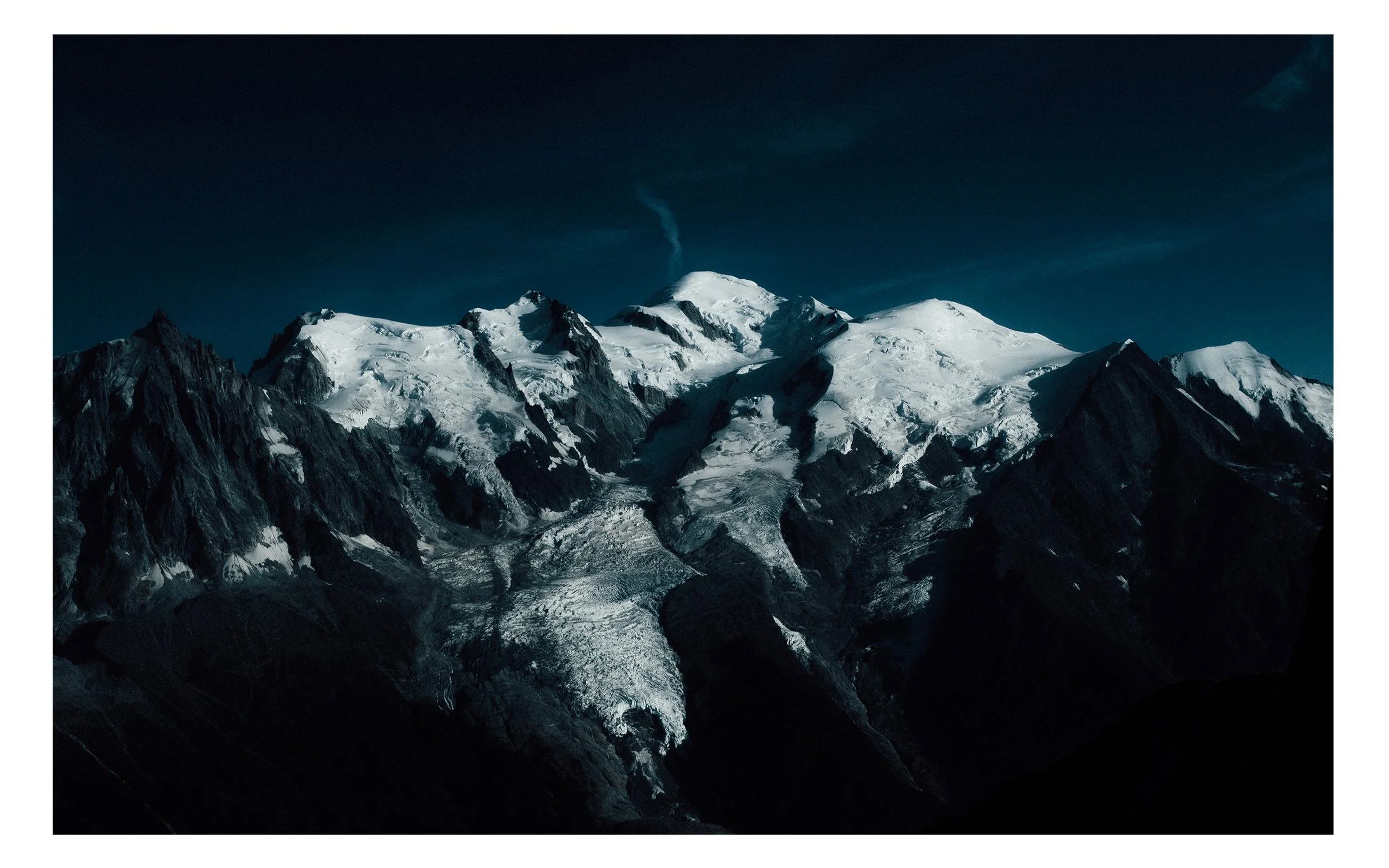 Montagnes enneigées avec un sommet principal et un ciel sombre.