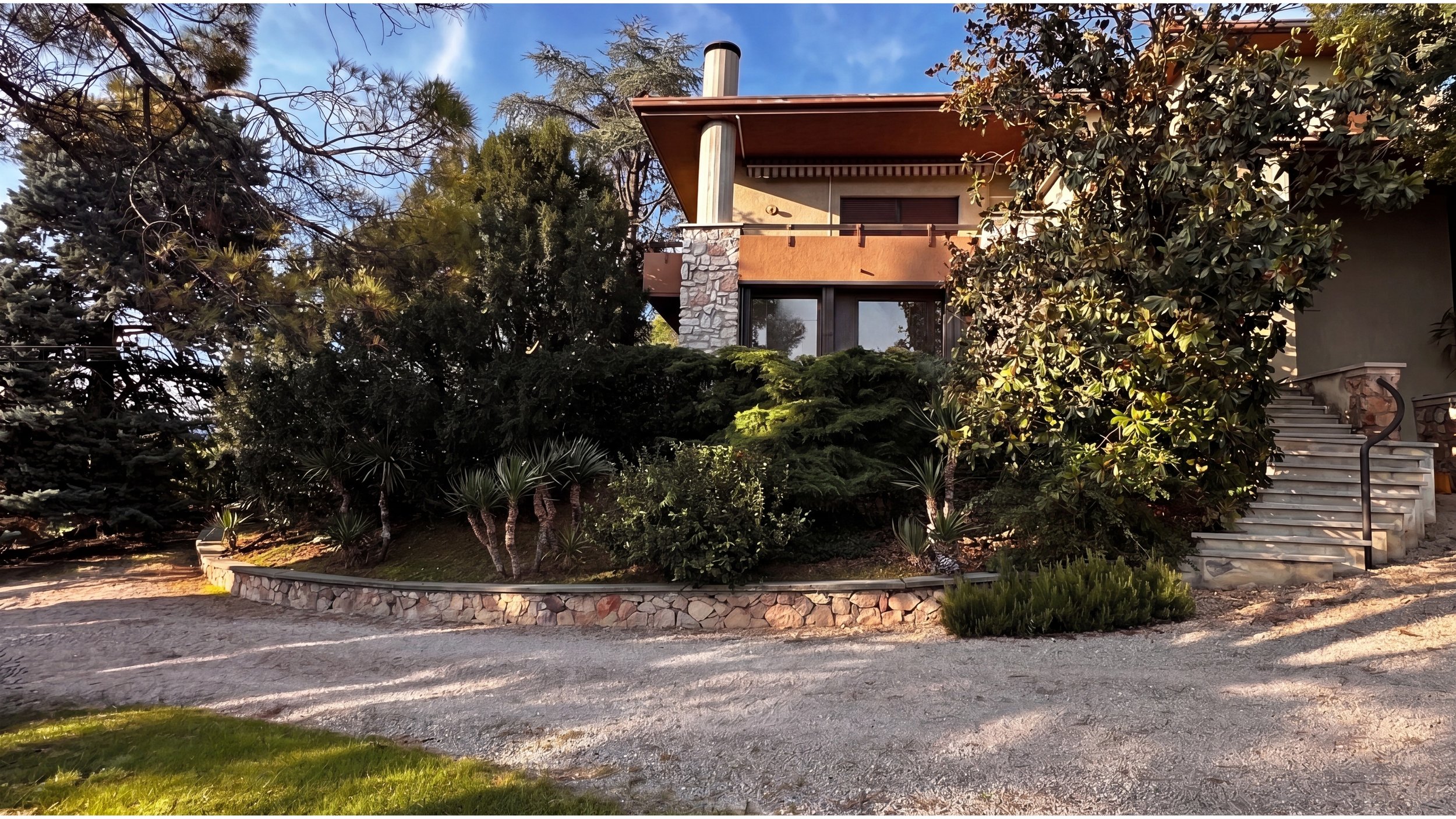 Villa degli Olivi: La parte di casa dove si trova l'appartamento n. 1. Un Edificio moderno e suggestivo con rivestimenti in pietra della lessinia, circondato da alberi e piante, con scale in pietra che portano all'ingresso.