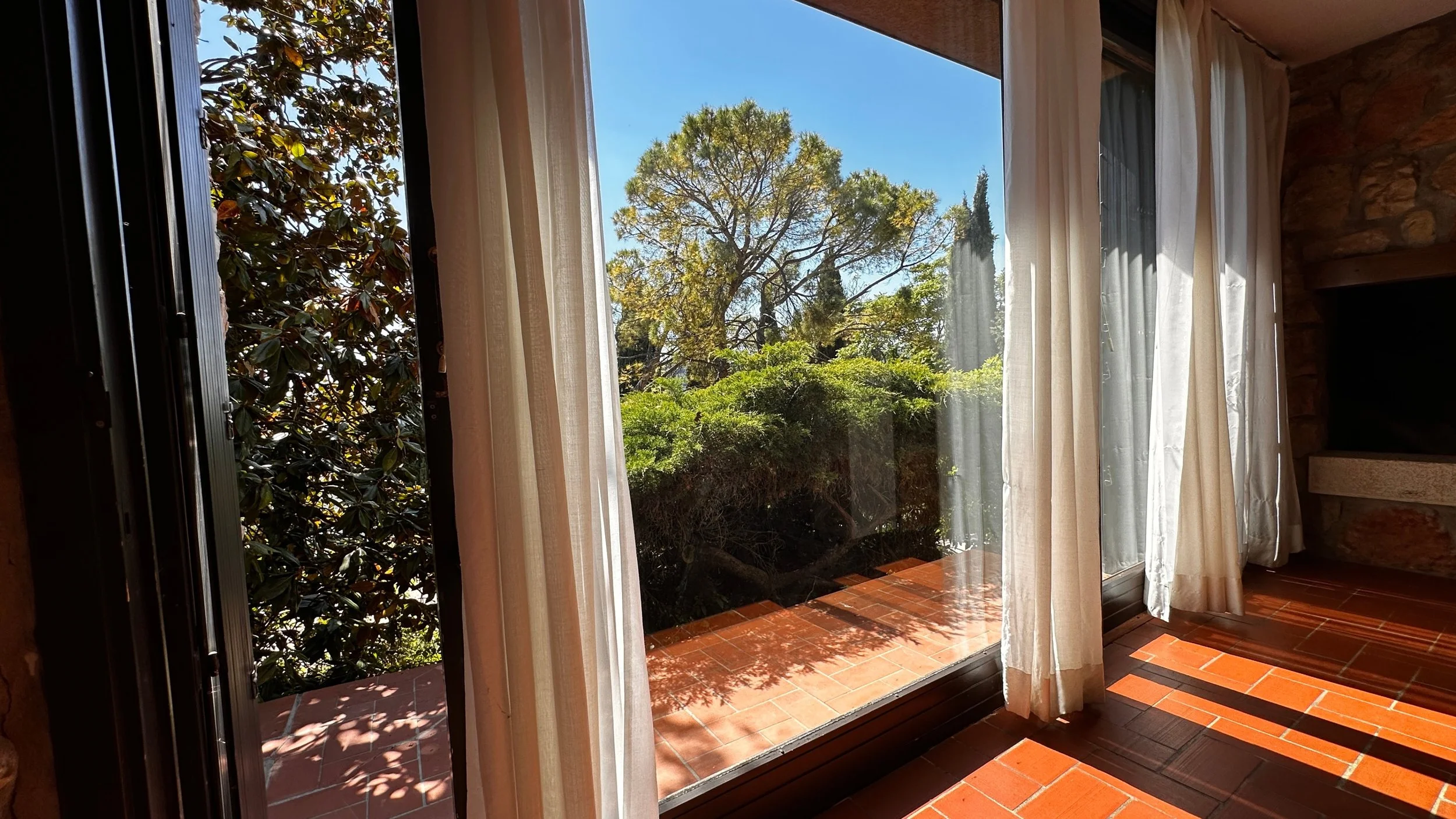 Vista panoramica dall'interno verso l'esterno dove la siepe e gli alberi fanno da cornice all'appartmamento impreziosito dal cotto e dalle pietre.