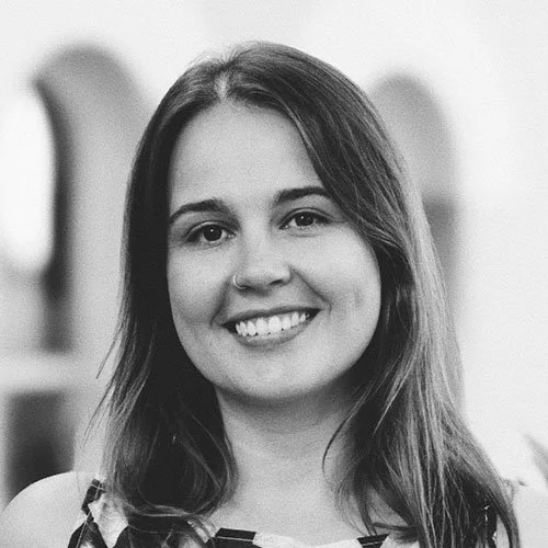 Black and white portrait of a young woman with long hair, smiling, in an outdoor setting.