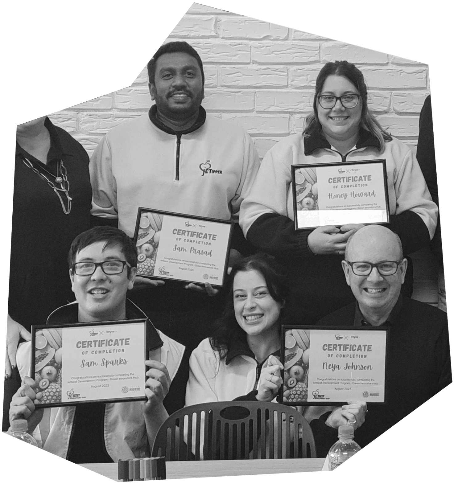 Group of smiling people holding certificates of completion at an indoor event, with a brick wall in the background.
