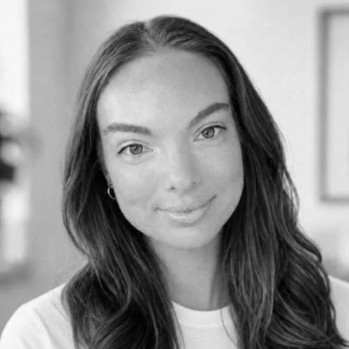 Black and white portrait of a young woman with long wavy hair, smiling softly, wearing a white shirt and small hoop earrings.