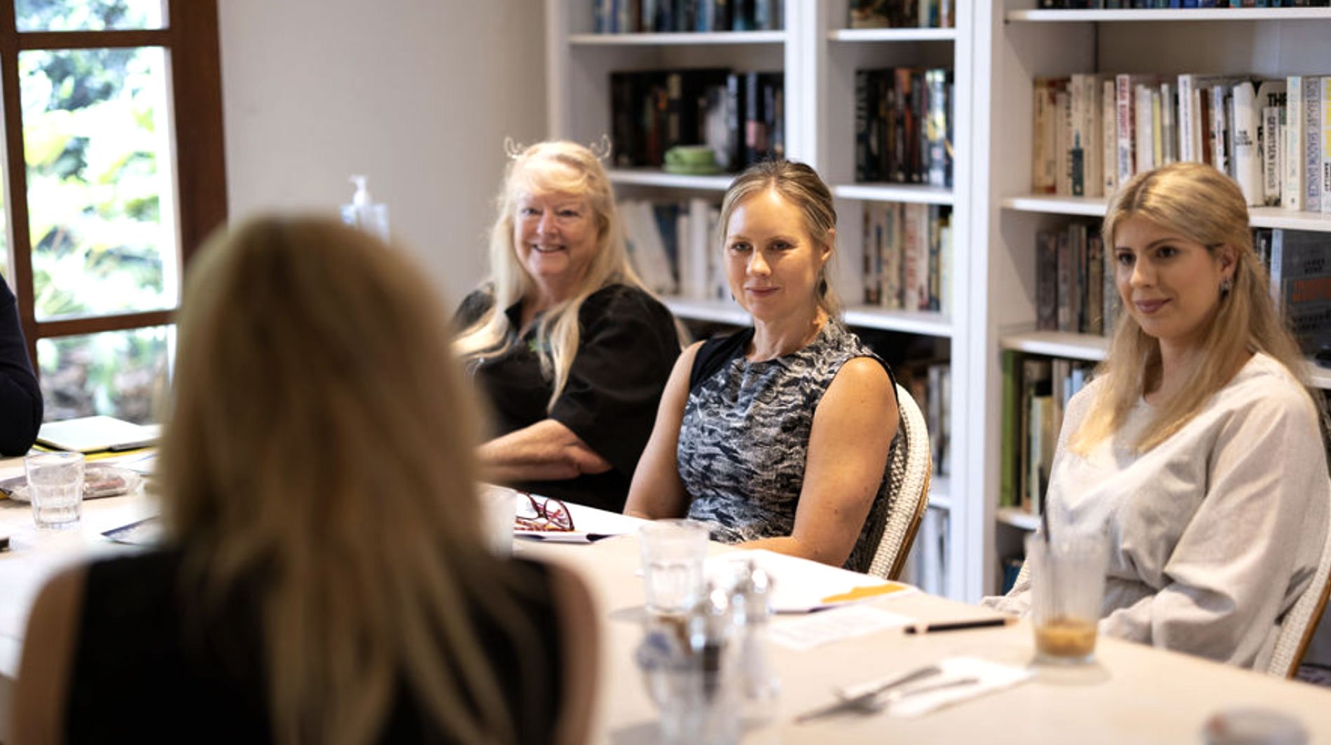 Group of women sitting around a table during a meeting in a library or office setting.