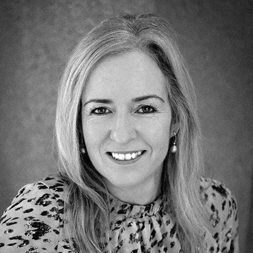Black and white portrait of a smiling woman with shoulder-length hair wearing a patterned top and earrings.