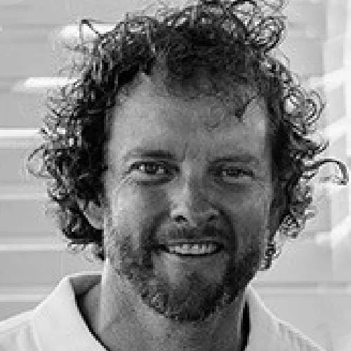 Black and white photo of a man with curly hair and a beard, smiling.